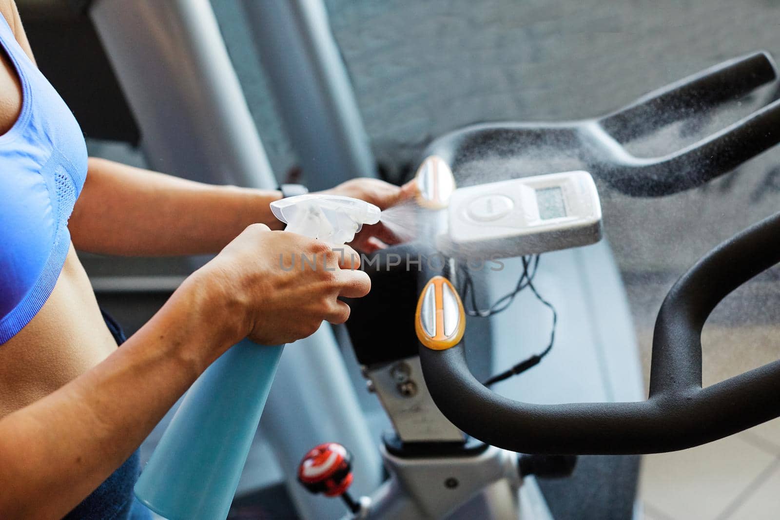 Young woman cleaning and weeping fitness gym equipment with sprayer