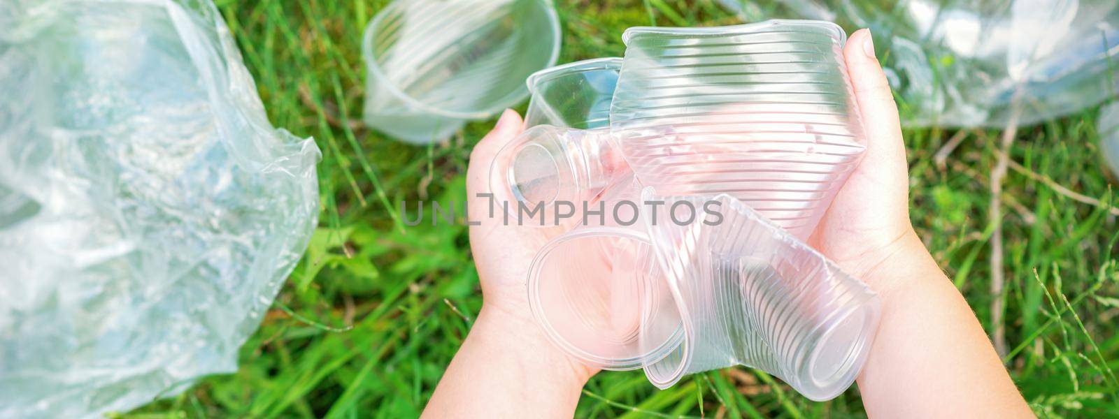 Child's hands clean the park from used plastic utensils in the grass