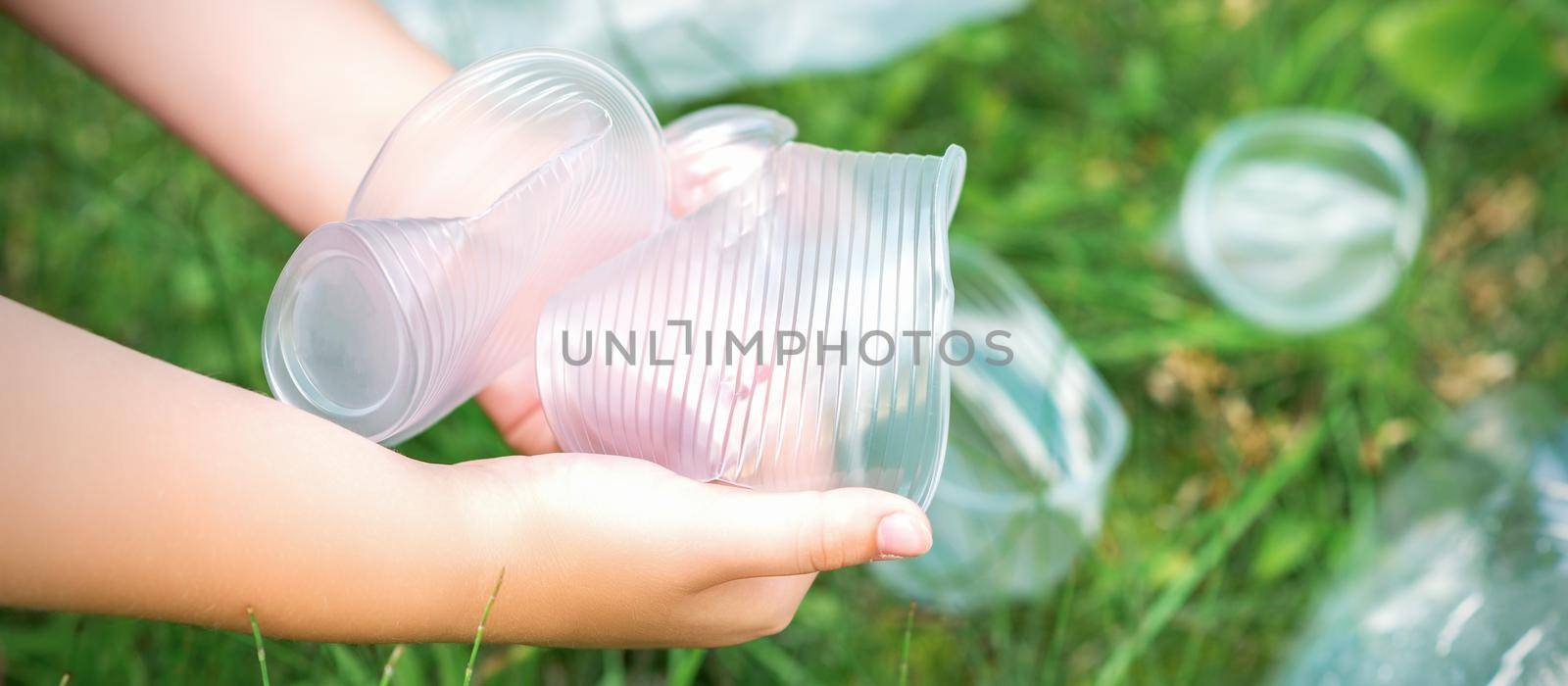 Child's hands clean the park from used plastic utensils in the grass