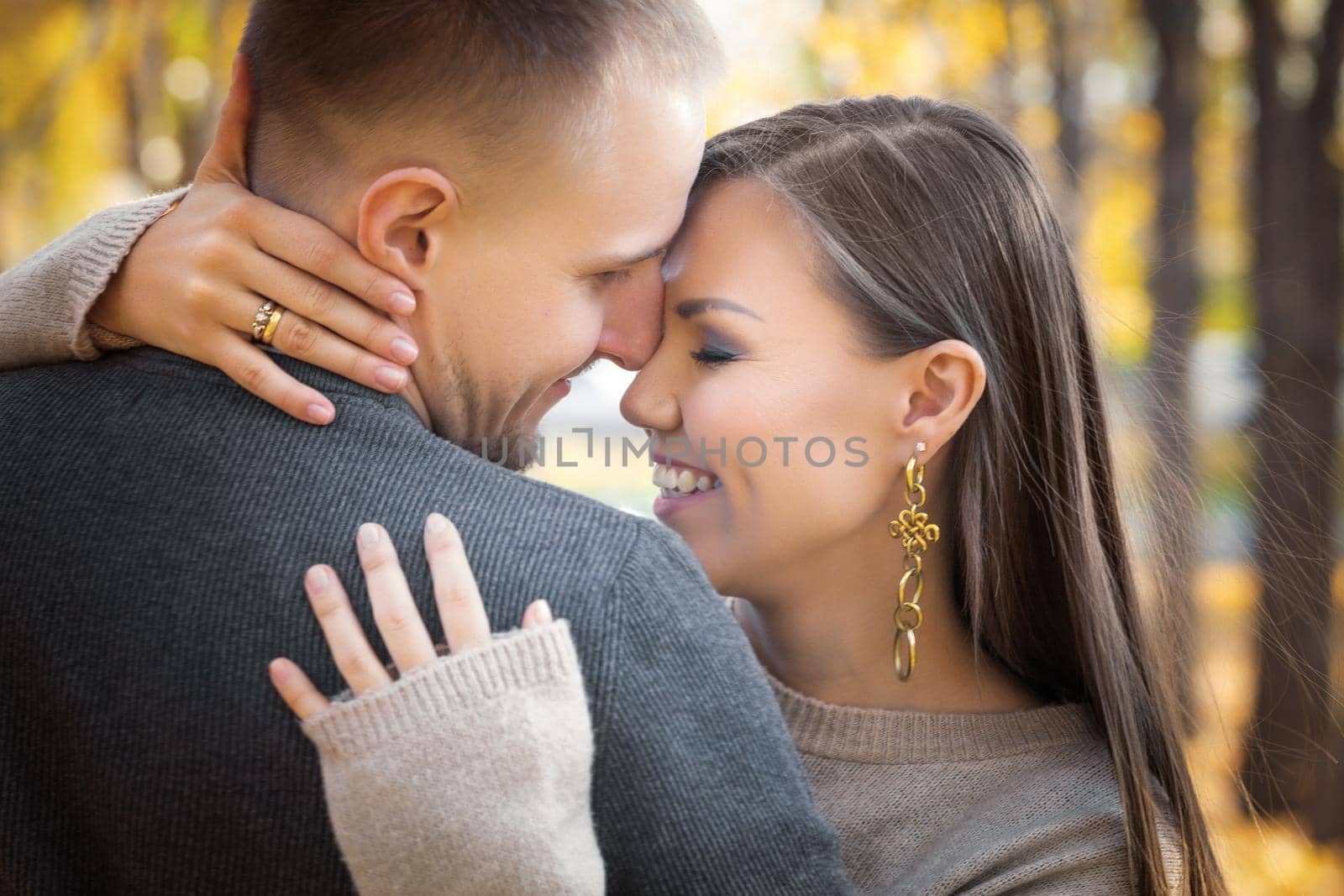 Happy smiling young Central Asian woman hugging her caucasian husband on a date in a autumn outdoor.