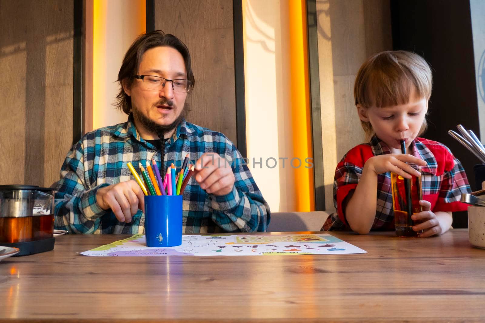 a child with his father in a restaurant draws a coloring book, waiting for cooking