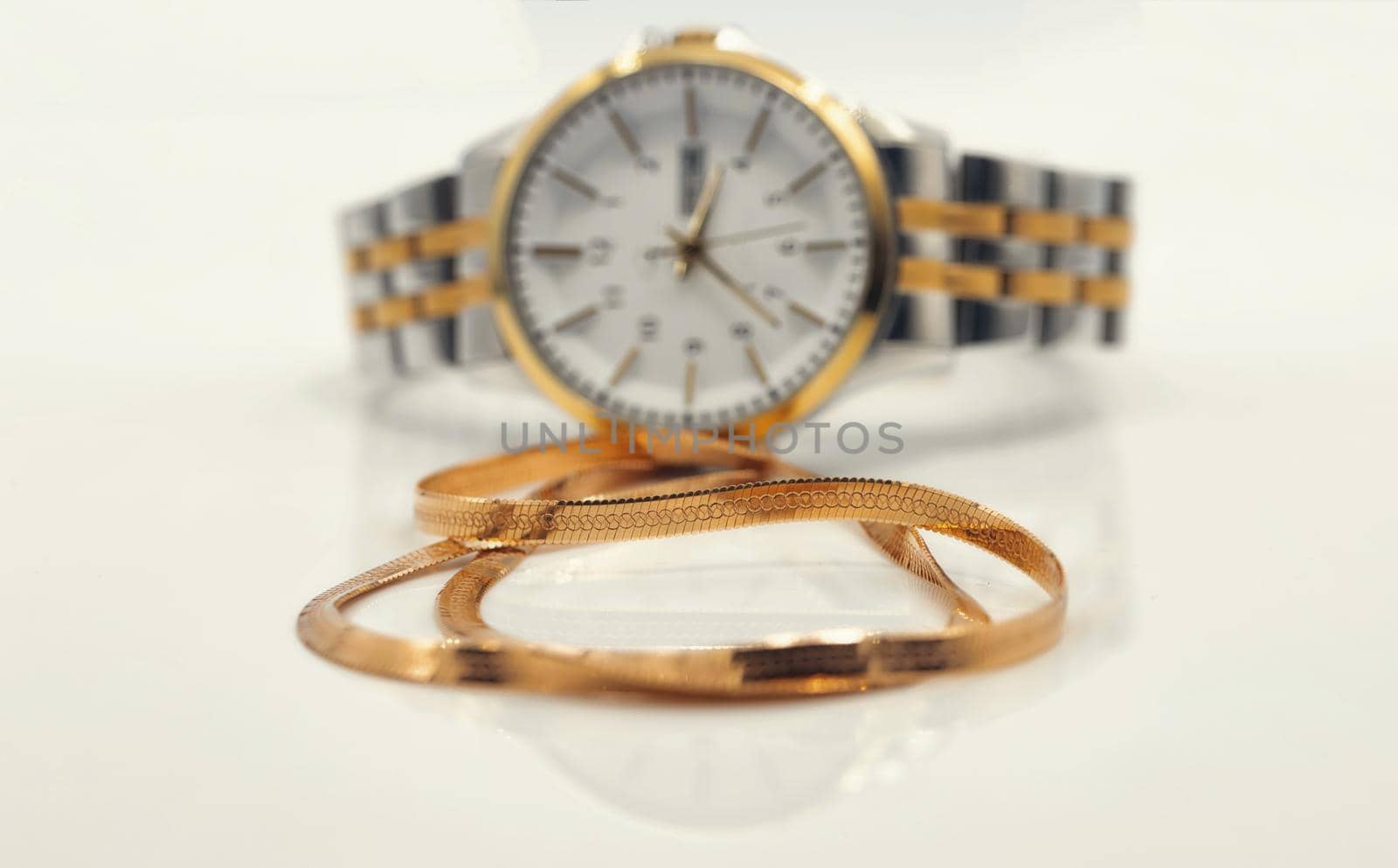 Elegant women's watch and gold chain with snakeskin weave lie on a white reflective surface