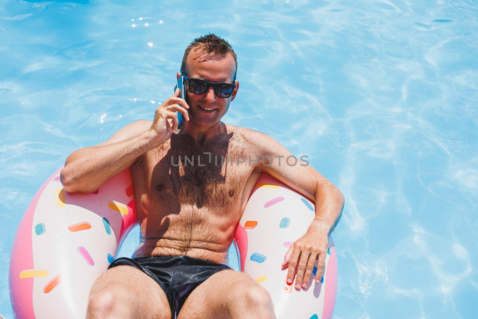 An attractive man is relaxing on an inflatable ring in the pool. A man in the pool is talking on the phone. vacation and free time concept