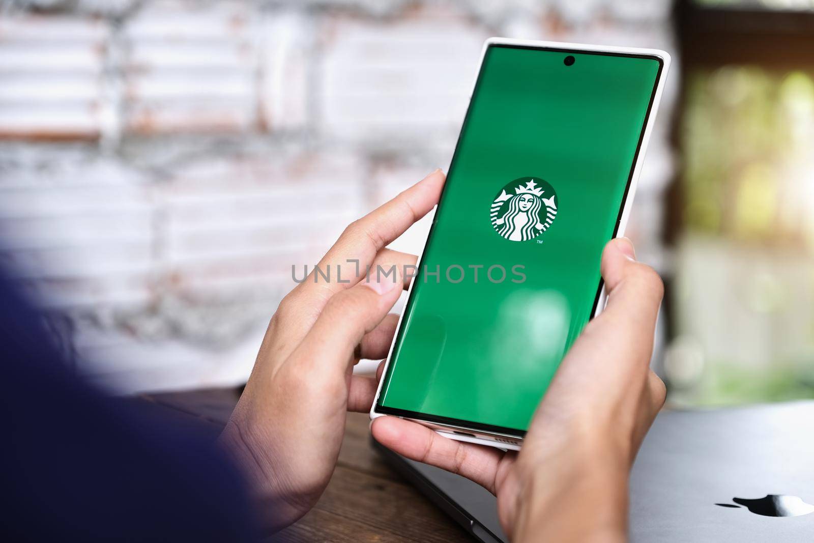 Chiang Mai, Thailand June 06, 2021:Woman hand holding smart phone mobile opening starbuck app by Manastrong