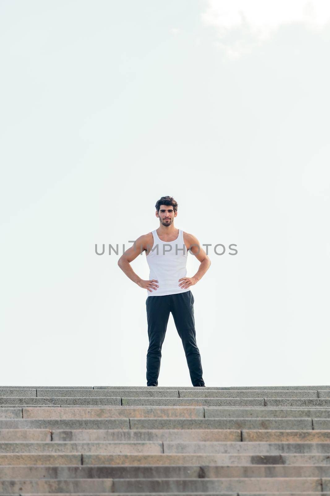 vertical photo of a handsome sportsman standing with his hands on his hips at the top of a staircase, concept of urban sport and healthy lifestyle, copy space for text