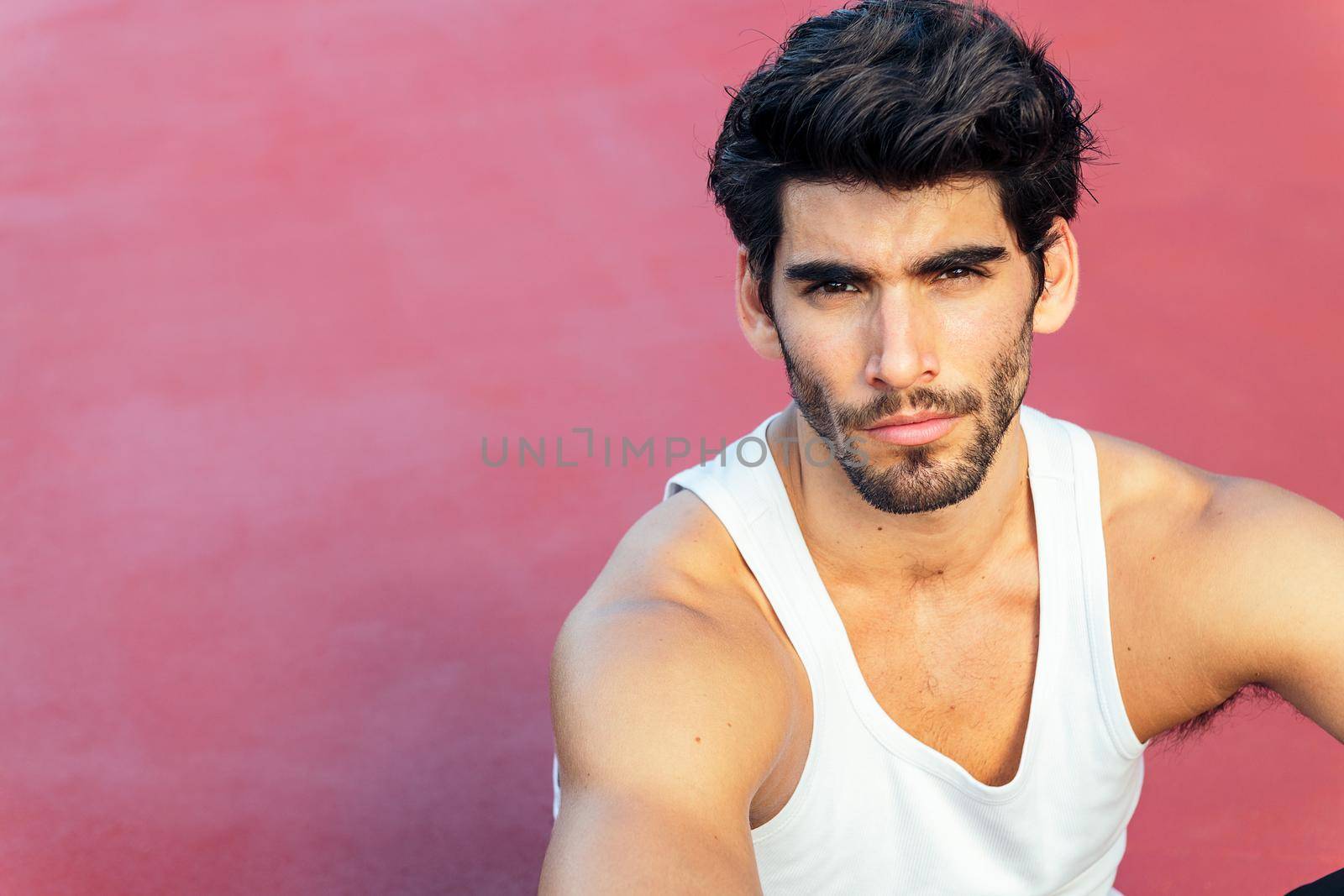 portrait of a handsome sportsman sitting on a red floor, concept of urban sport and healthy lifestyle, copy space for text