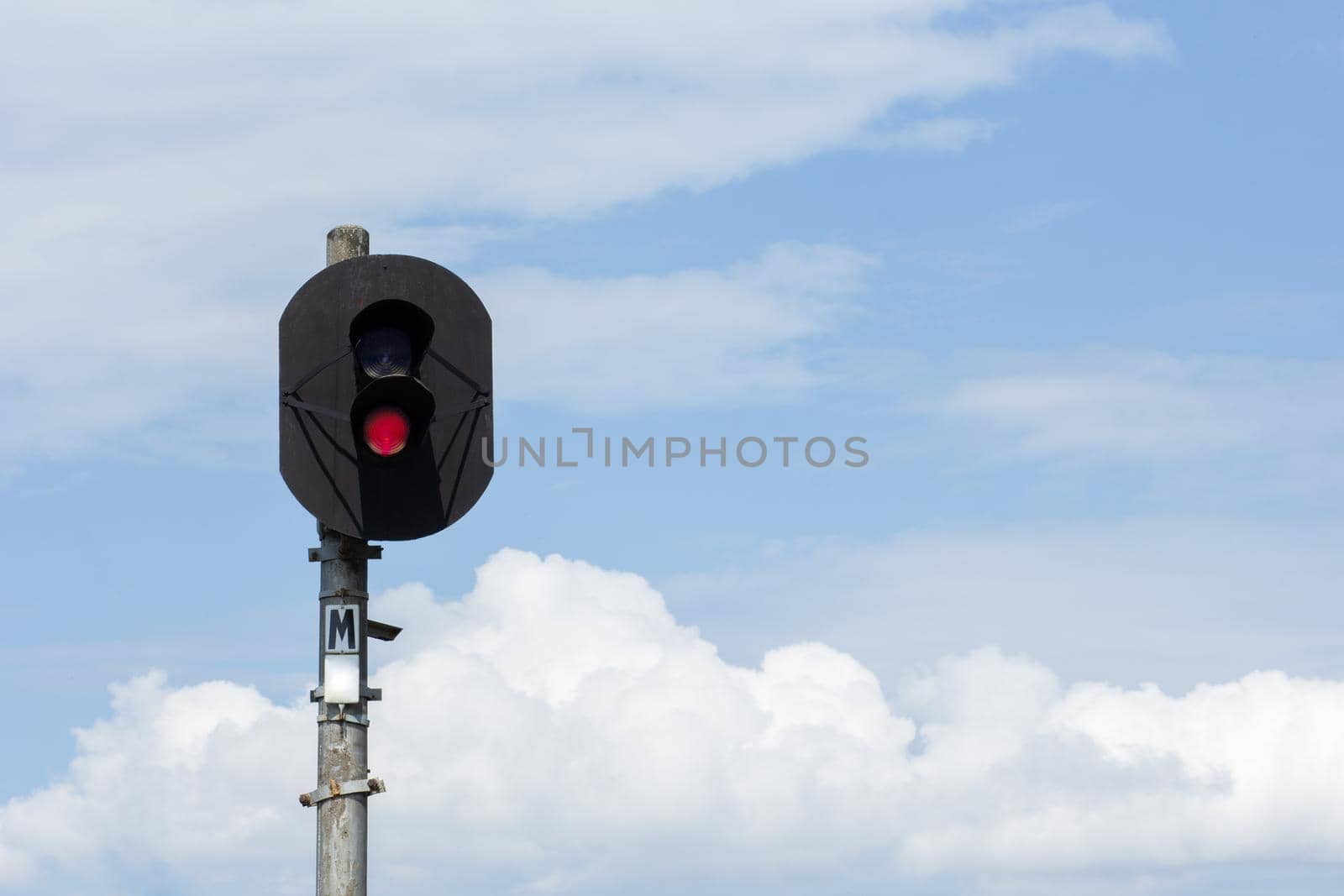 Two-aspect colour light railway signal with displayed red light set at danger and to stop over blue sky