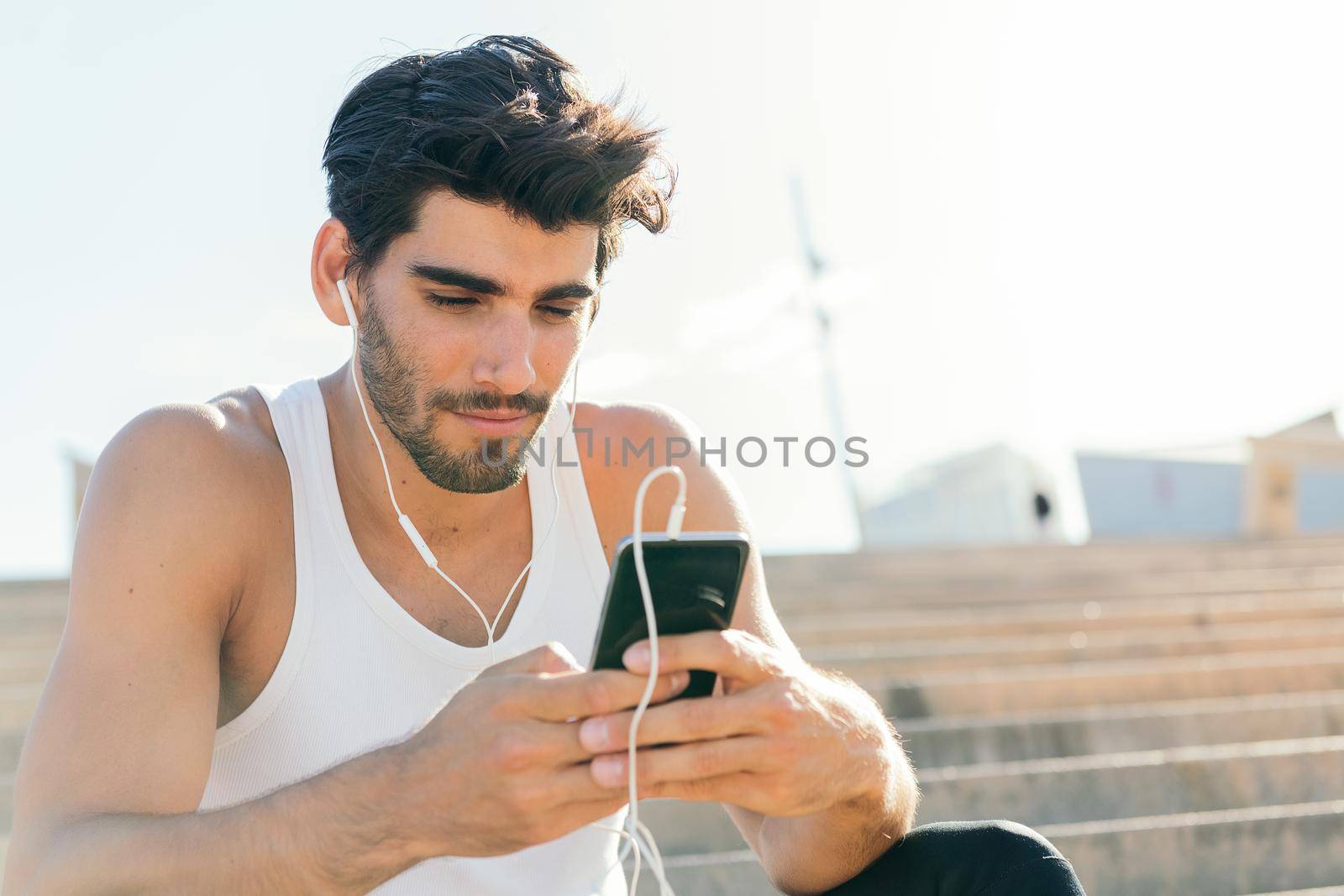 handsome sporty man with earphones selects music on his phone to listen during his workout, urban sport concept and healthy lifestyle, copy space for text