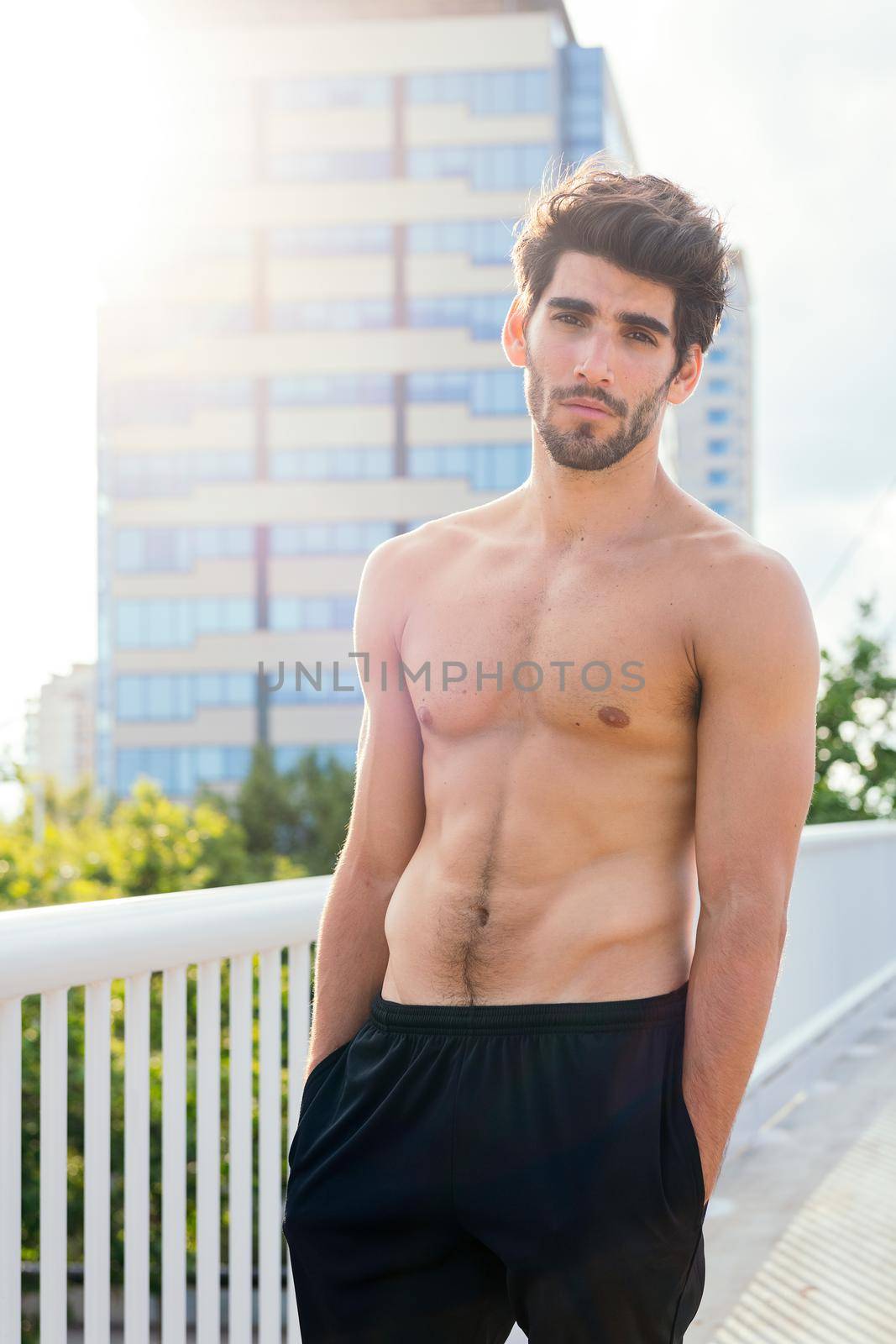 vertical photo of a handsome shirtless sportsman posing in front of city buildings, concept of urban sport and healthy lifestyle, copy space for text