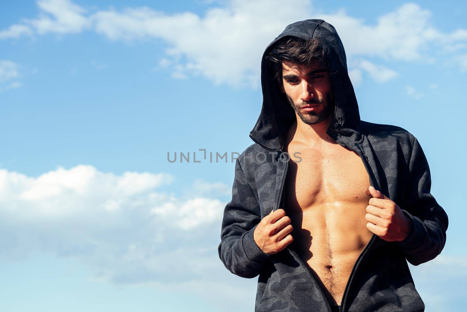 handsome sportsman showing off his muscles under a hooded sweatshirt, concept of sport and healthy lifestyle, copy space for text
