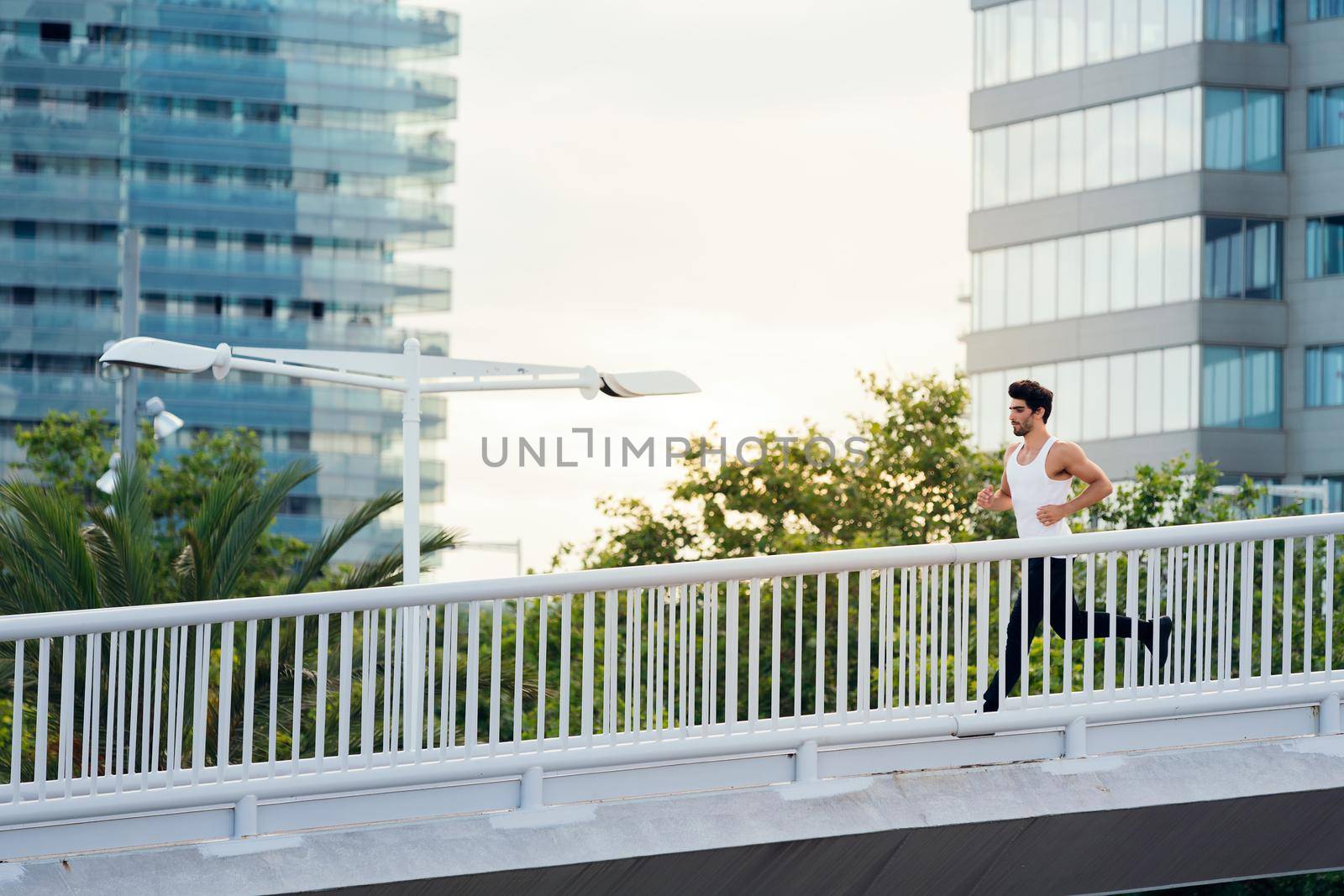 sporty man running on a city bridge in front of buildings, concept of urban sport and healthy lifestyle, copy space for text