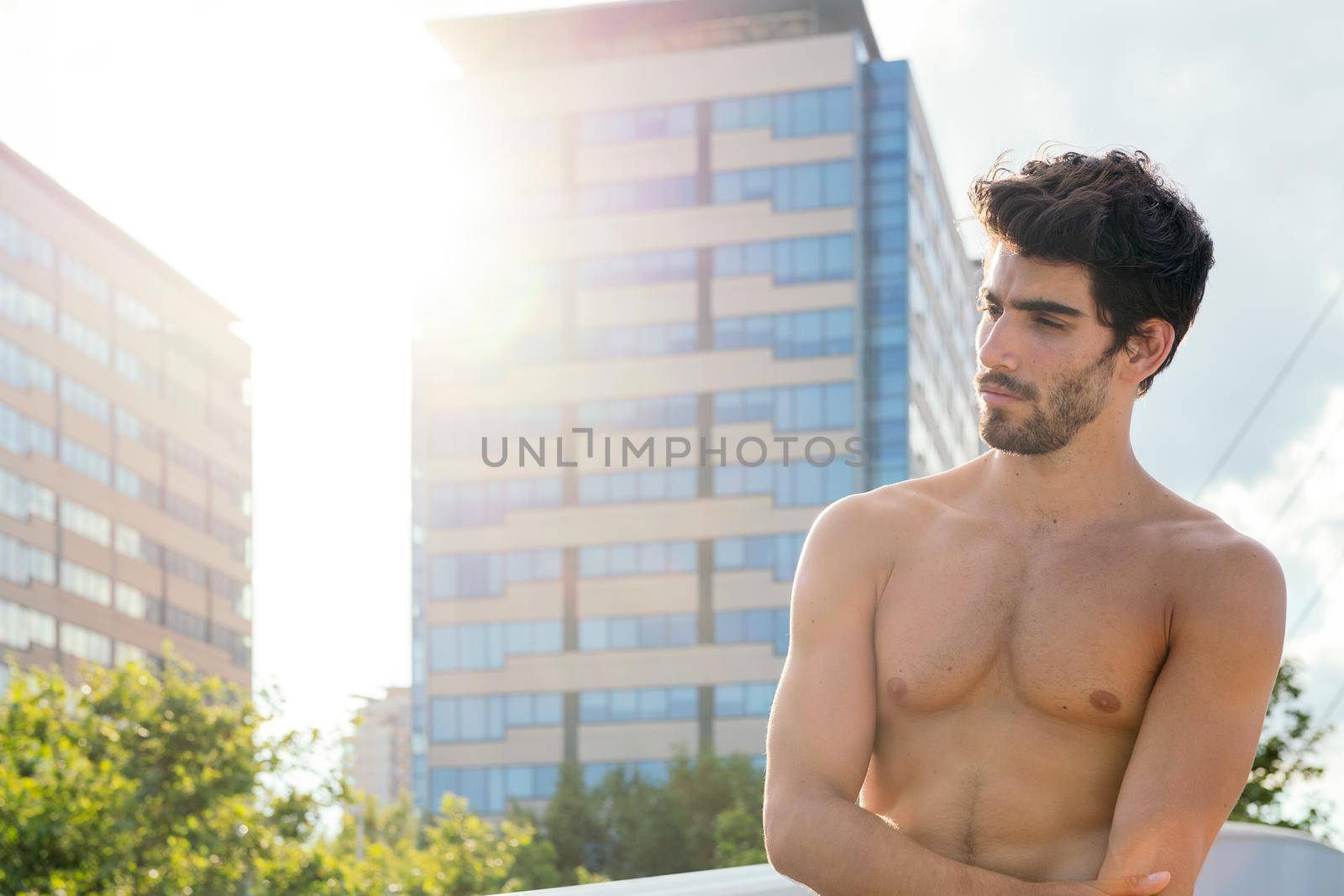 handsome shirtless sportsman posing at sunshine in front of city buildings, concept of urban sport and healthy lifestyle, copy space for text