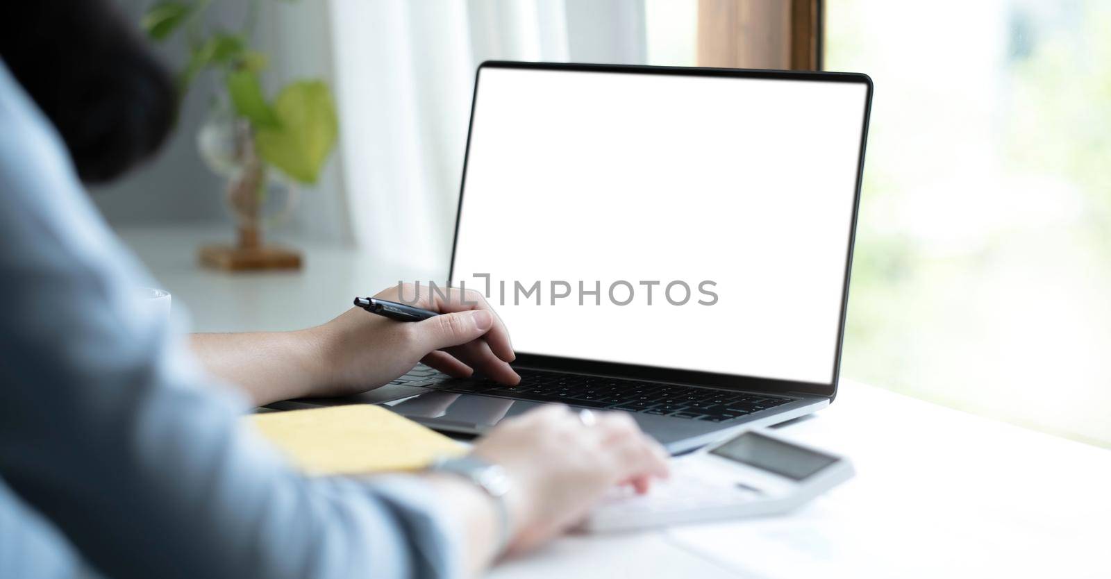 Mockup image of a woman using laptop with blank white screen on wooden table in office by wichayada