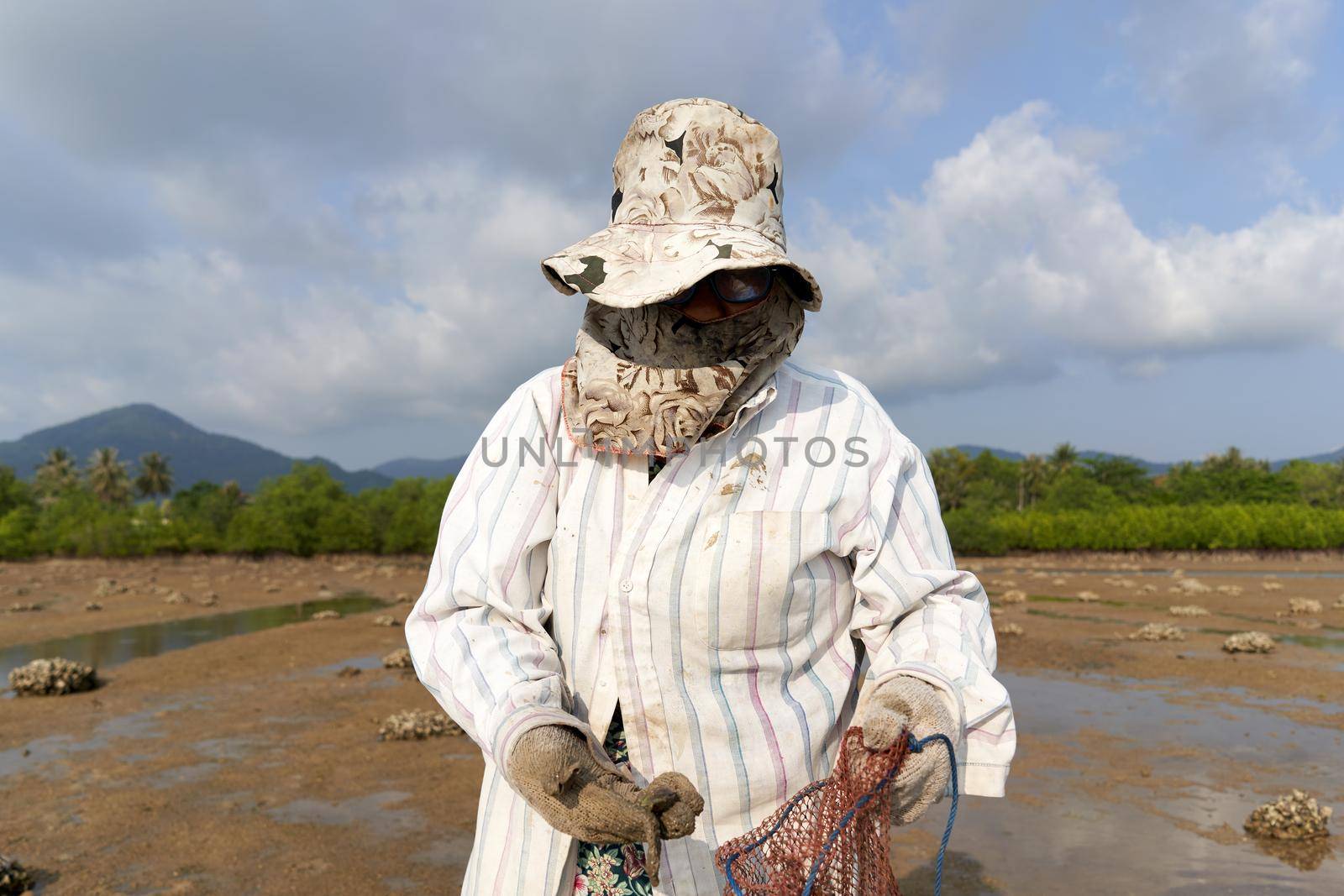 Ko Phangan, Thailand, March 15, 2022: covered woman looking for clams on the sea by WesternExoticStockers