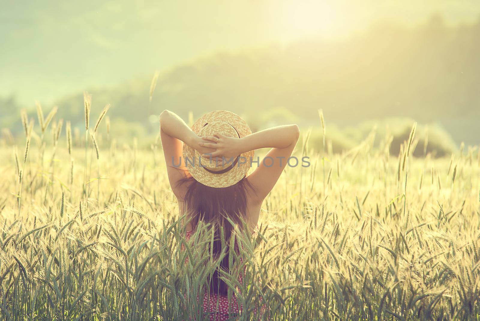 young woman in straw hat in the middle of wheat field enjoing summertime