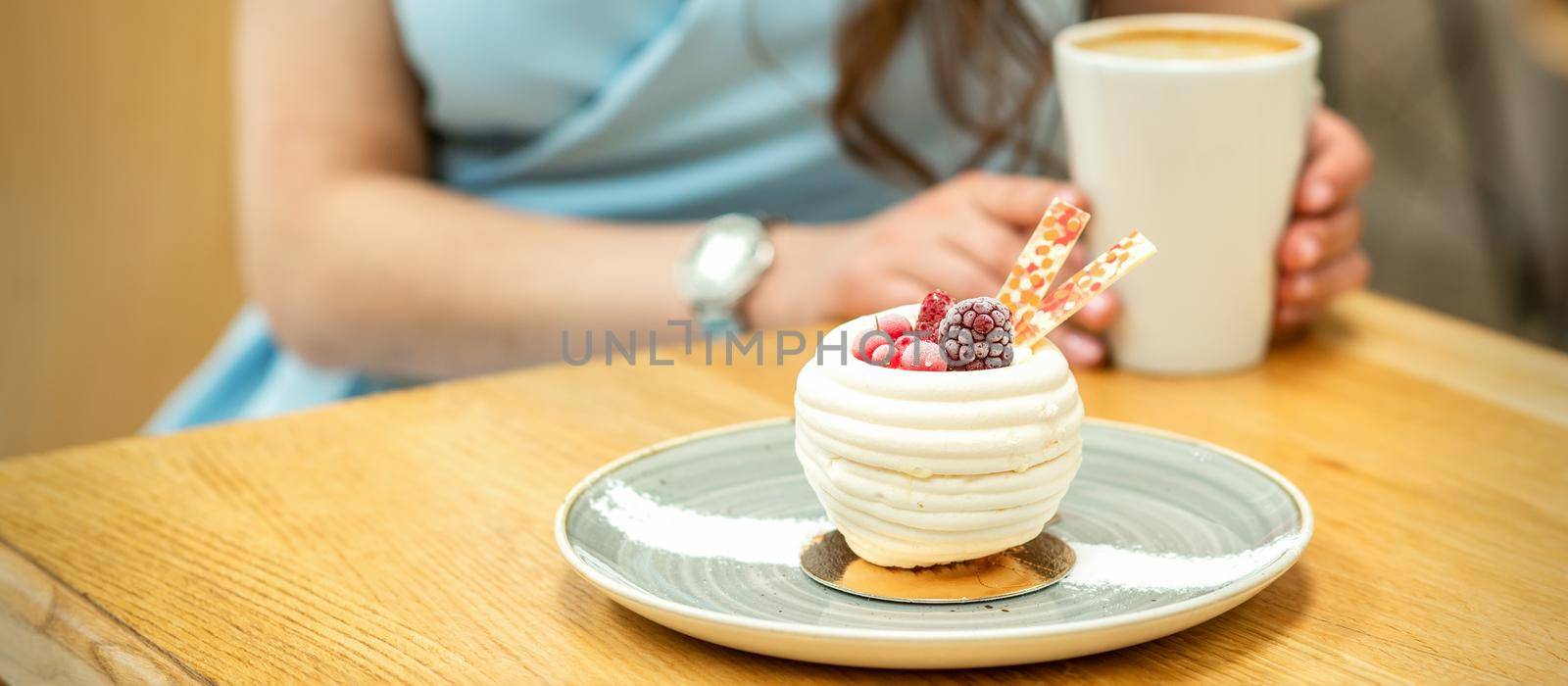 Sweet white cupcake with berries on the plate at the table on a woman's background with a cup of coffee in a cafe