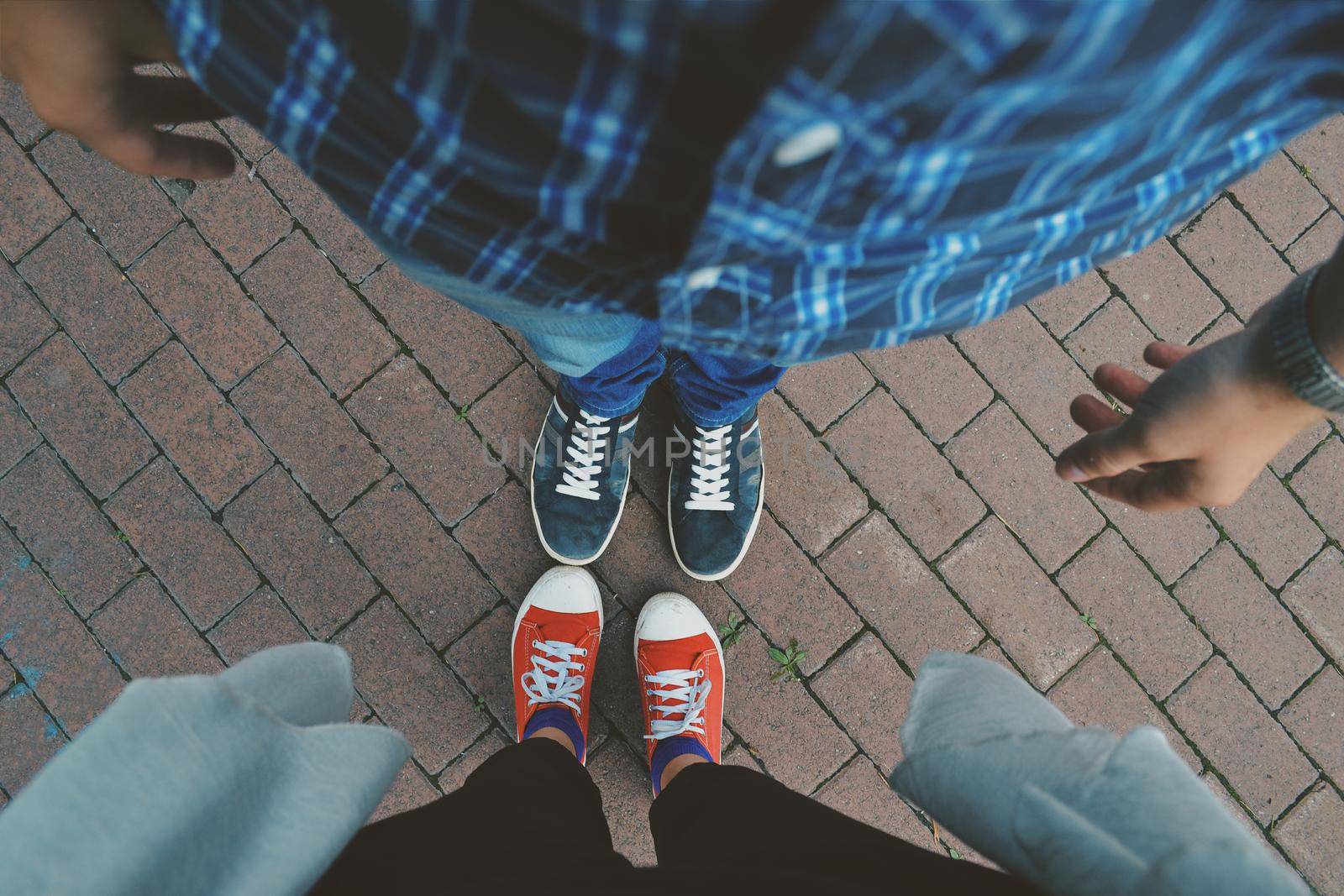 Photo of the legs of a man and a woman in blue and red sneakers with white laces on a paved path by ProjectStockman