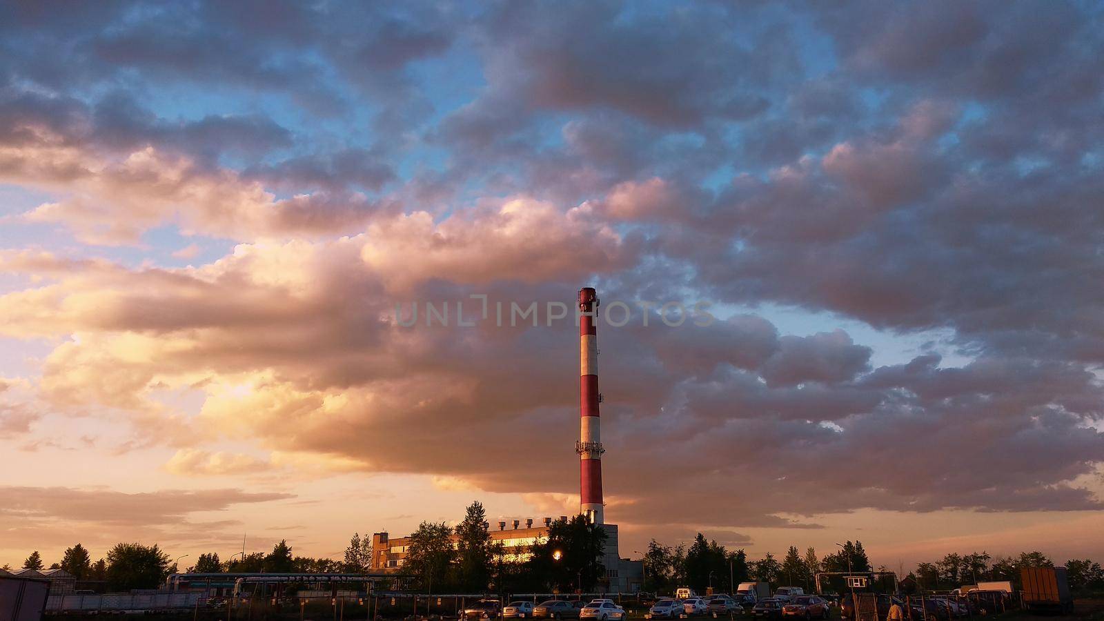 Chimney of a boiler house against the background of a cloudy evening sky in the light of the setting sun by ProjectStockman