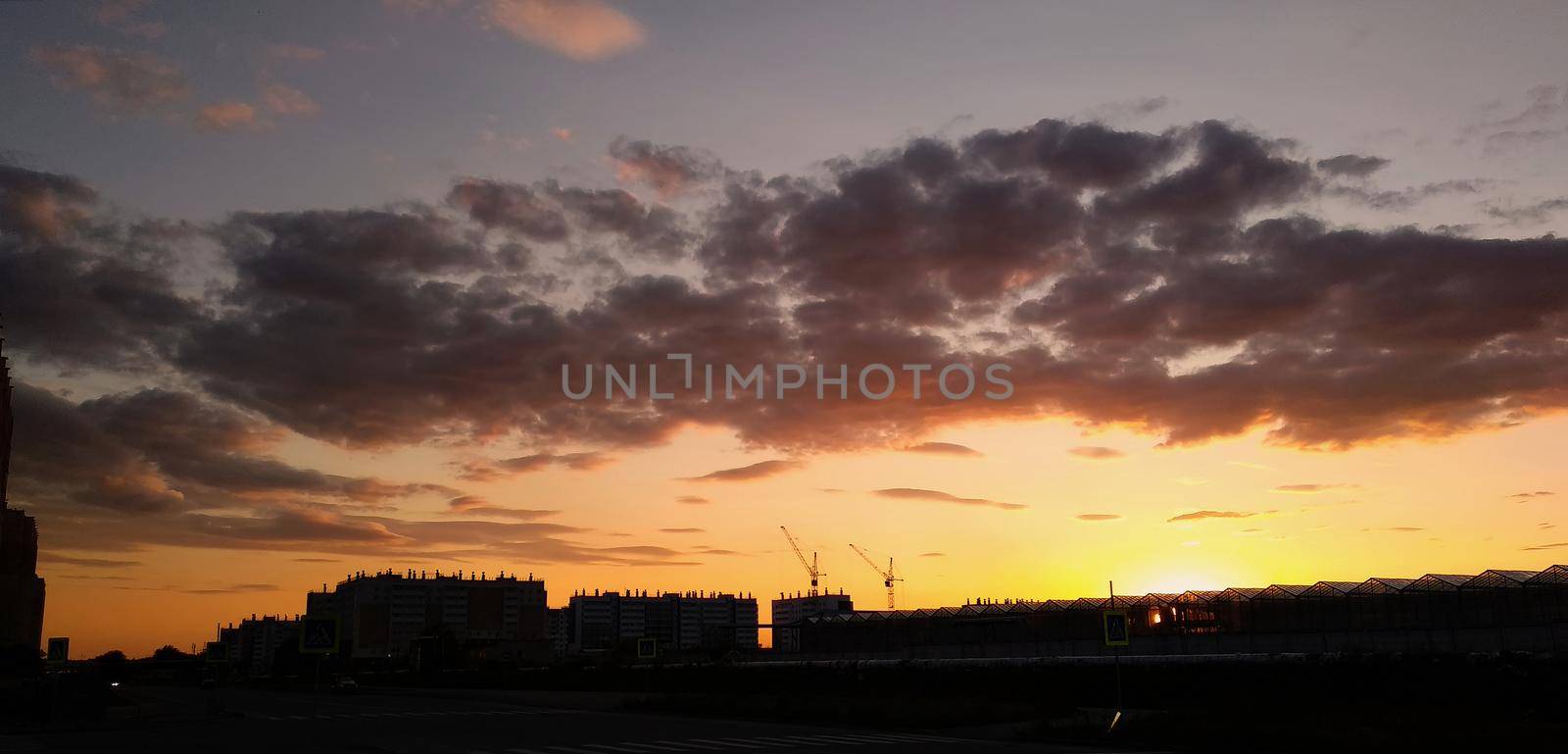 Clouds in the evening orange sky against the background of the setting sun and silhouettes of buildings by ProjectStockman