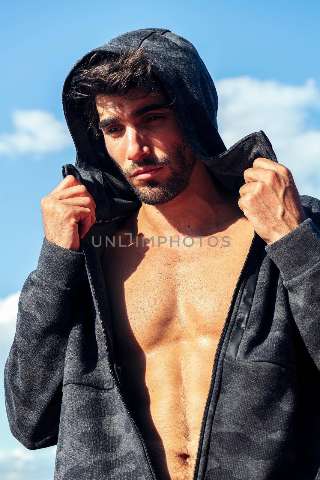 vertical photo of a handsome sportsman showing off his muscles under a hooded sweatshirt, concept of sport and healthy lifestyle