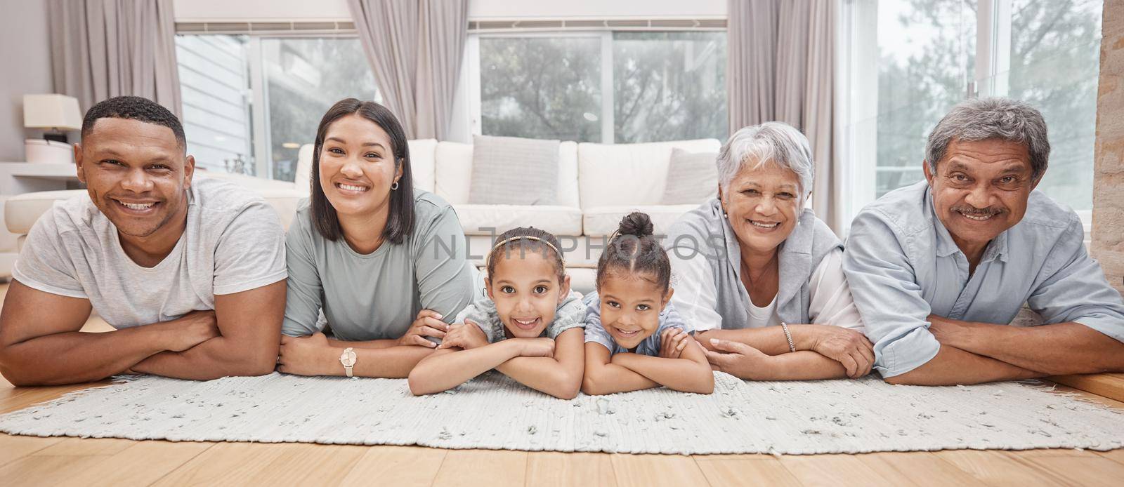 Happy and affectionate young mixed race family of six lying on the living room floor at home. Married couple with their mother, father and two cute daughters in the lounge. Granny and grandpa visit.