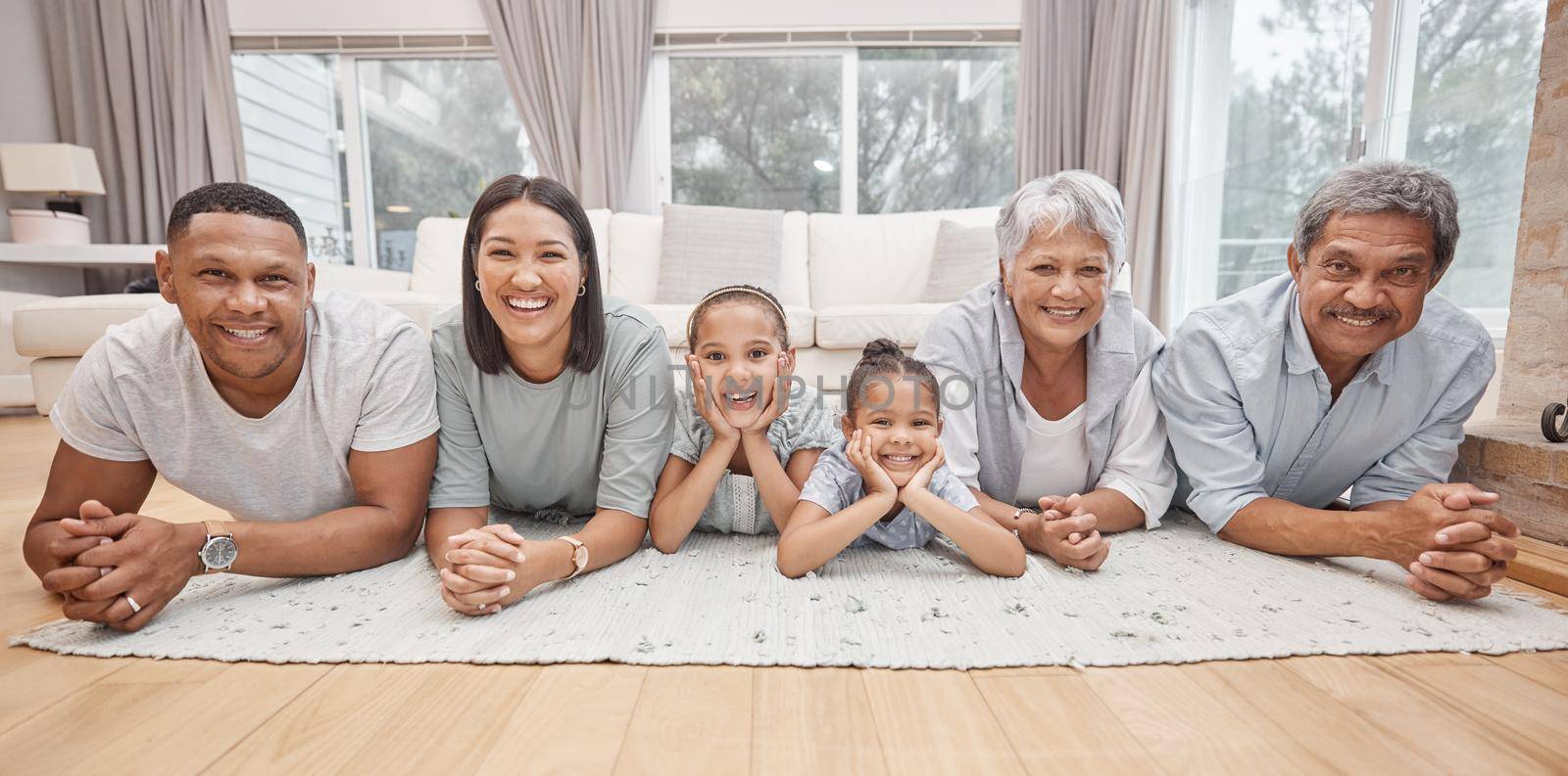 Happy and affectionate young mixed race family of six lying on the living room floor at home. Married couple with their mother, father and two cute daughters in the lounge. Granny and grandpa visit by YuriArcurs