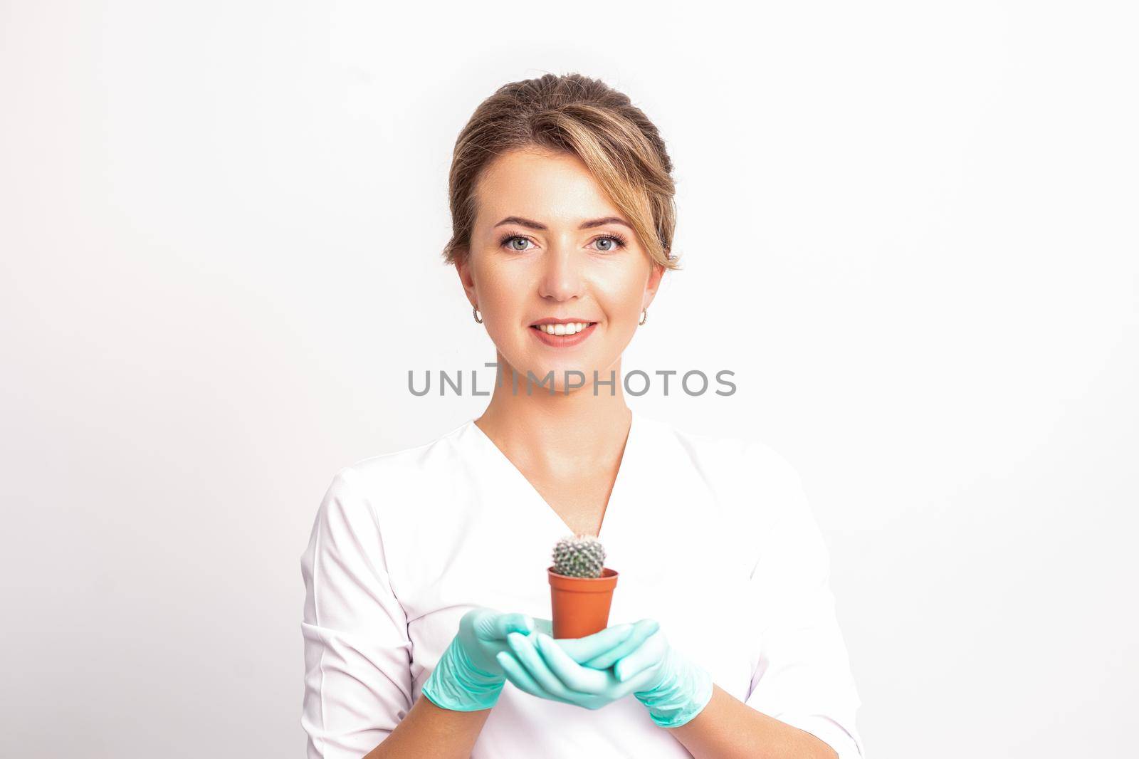 Young beautiful smiling female beautician holding a small cactus in a pot on white background