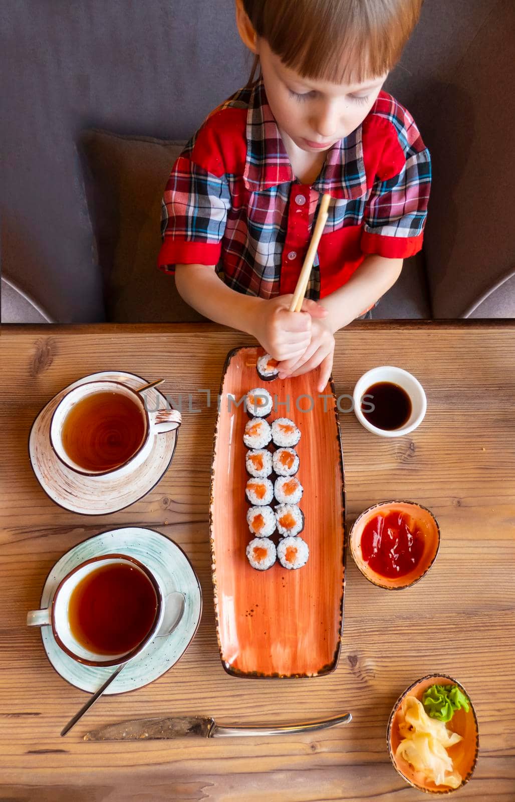 Little cute little boy eating sushi in a cafe, concept of eating. the boy in the restaurant eats sushi, dumbly holding chopsticks. View from aboveHigh quality photo