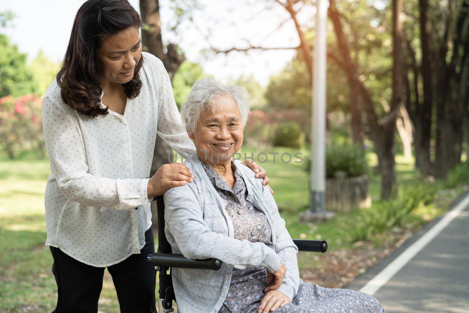 Caregiver help and care Asian senior or elderly old lady woman patient sitting and happy on wheelchair in park, healthy strong medical concept.
