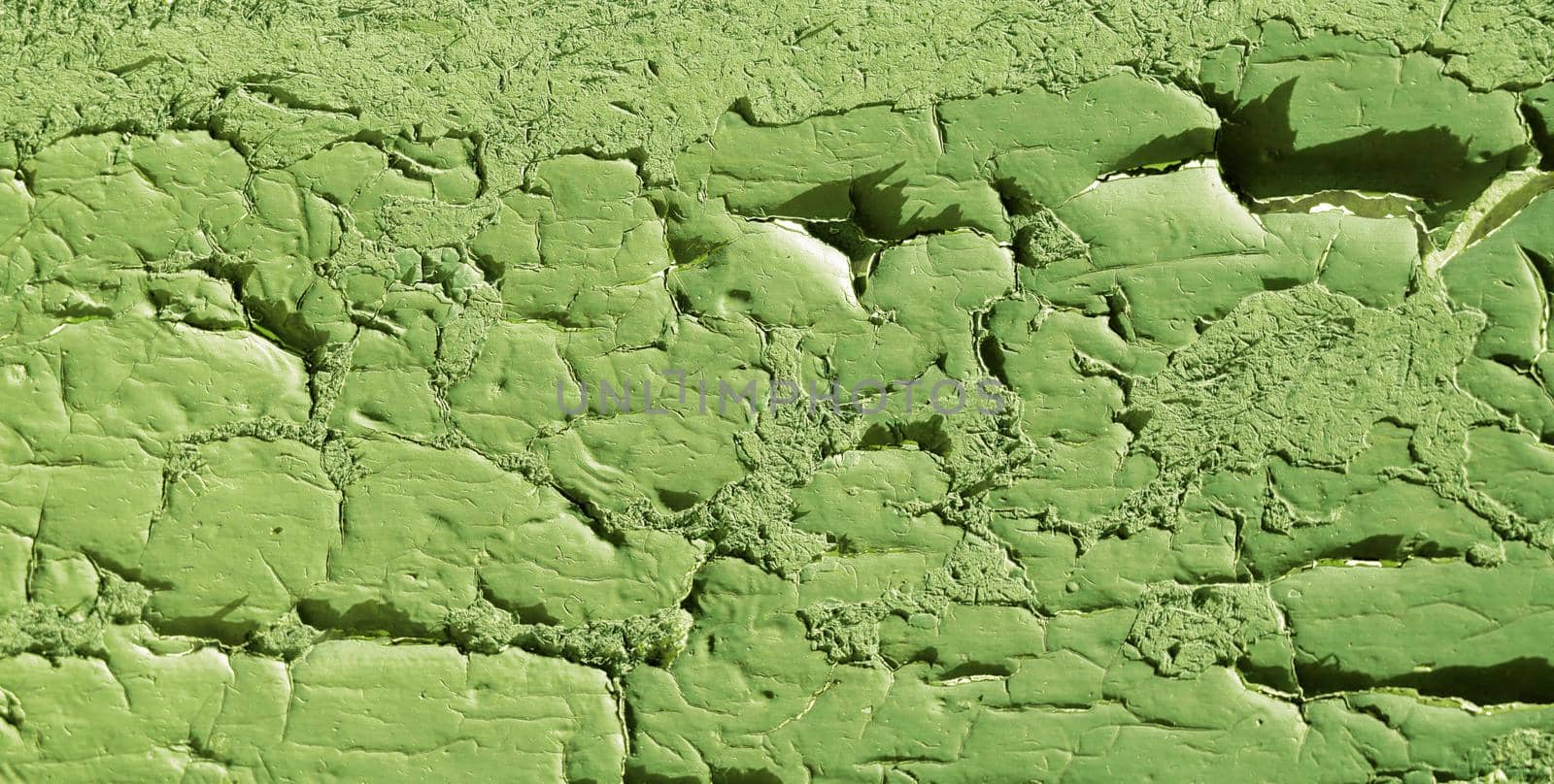 Abstract background of old damaged wood surface covered with green paint. Texture of large cracks and damage on wall.