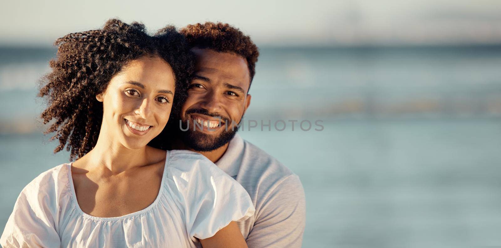 Closeup portrait of an young affectionate mixed race couple standing on the beach and smiling during sunset outdoors. Hispanic couple showing love and affection on a romantic date at the beach.
