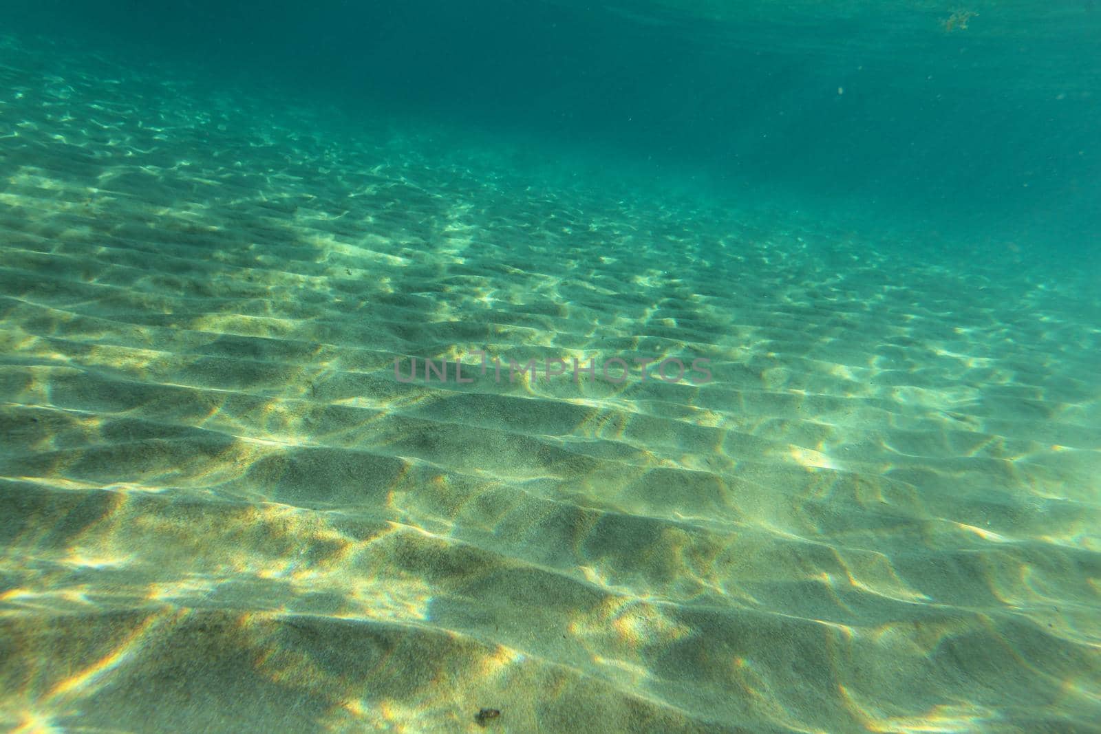 Sea bottom near sandy beach, sun lights on sand "dunes". Underwater photo, abstract marine background.