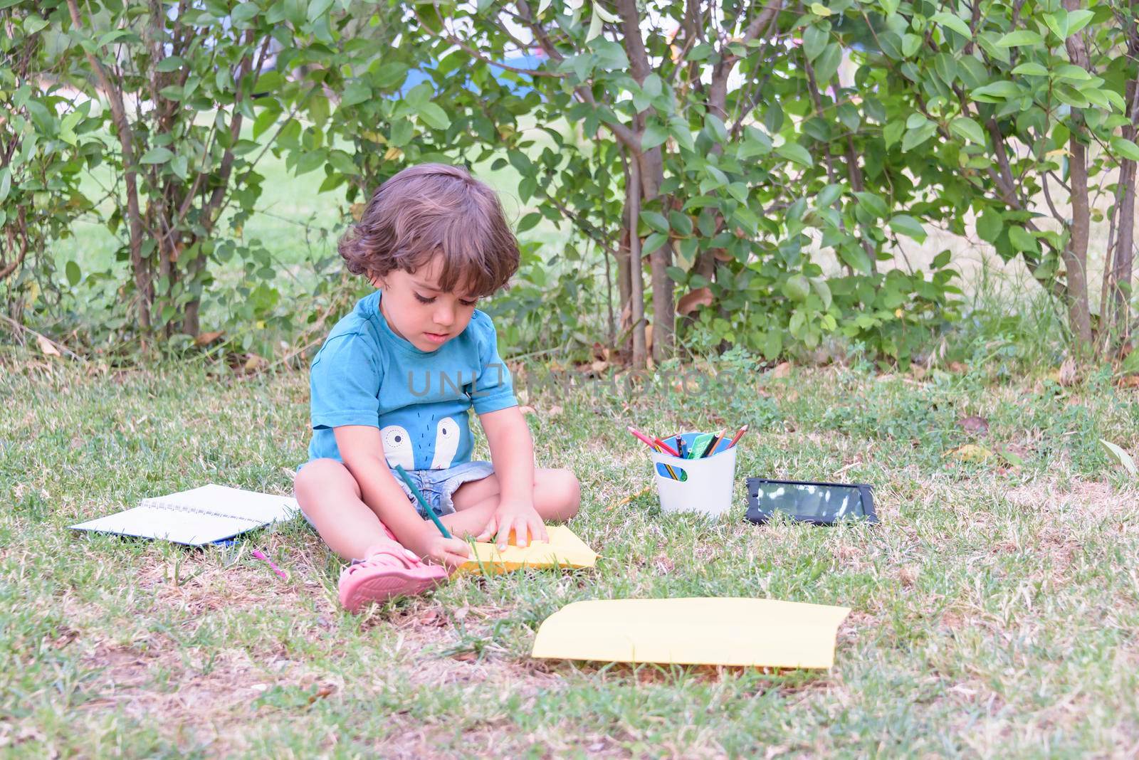 Little boy are using a magic pen to draw pictures in a book on a wooden table in park With face expression of determination