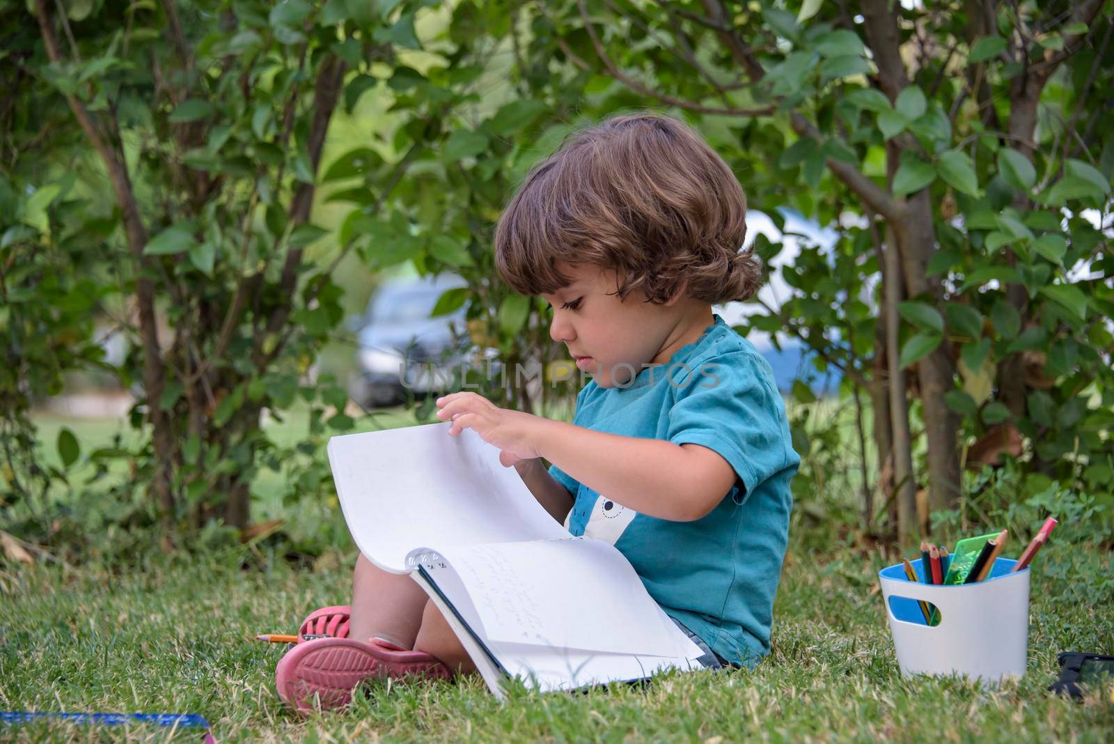 Little boy are using a magic pen to draw pictures in a book on a wooden table in park With face expression of determination