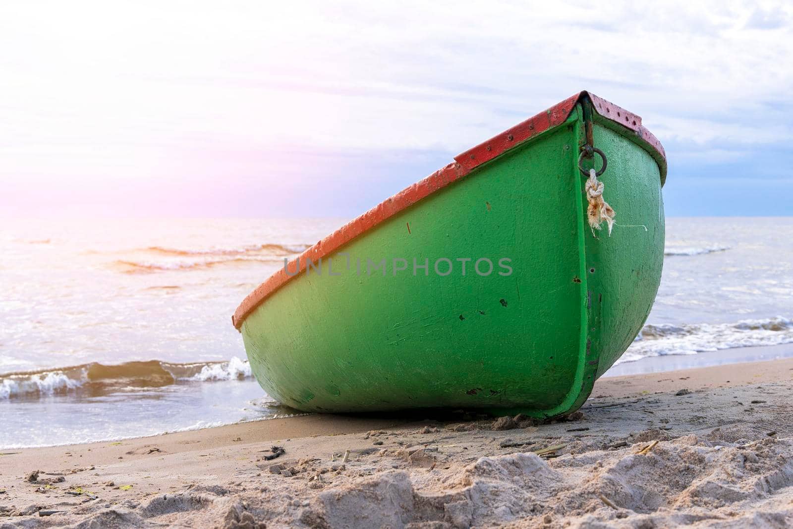 a green wooden fishing boat pulled onto the sand of the shore of the sea bay. a small pleasure boat on the shore of the bay in the setting sun.