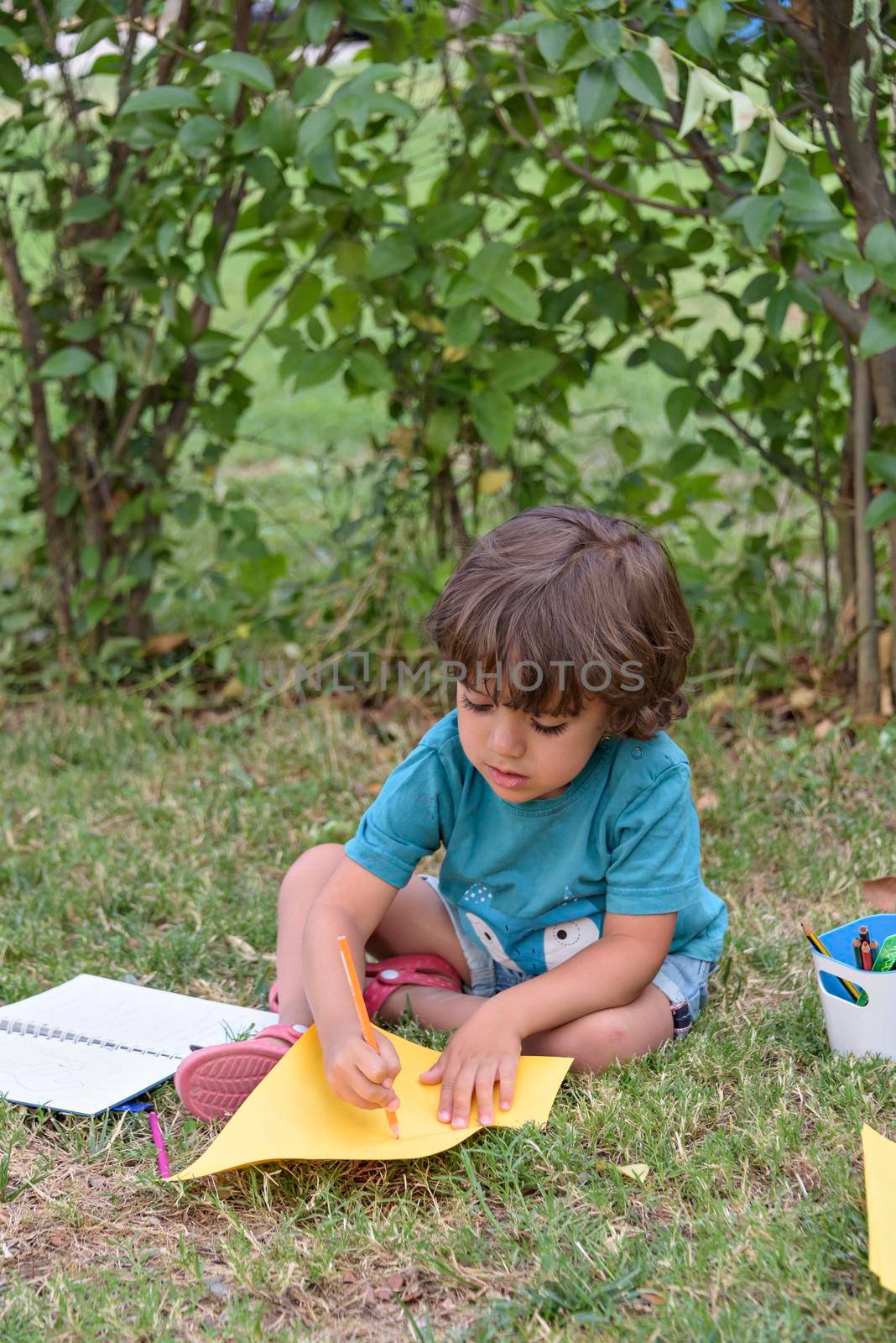 Little boy are using a magic pen to draw pictures in a book on a wooden table in park With face expression of determination