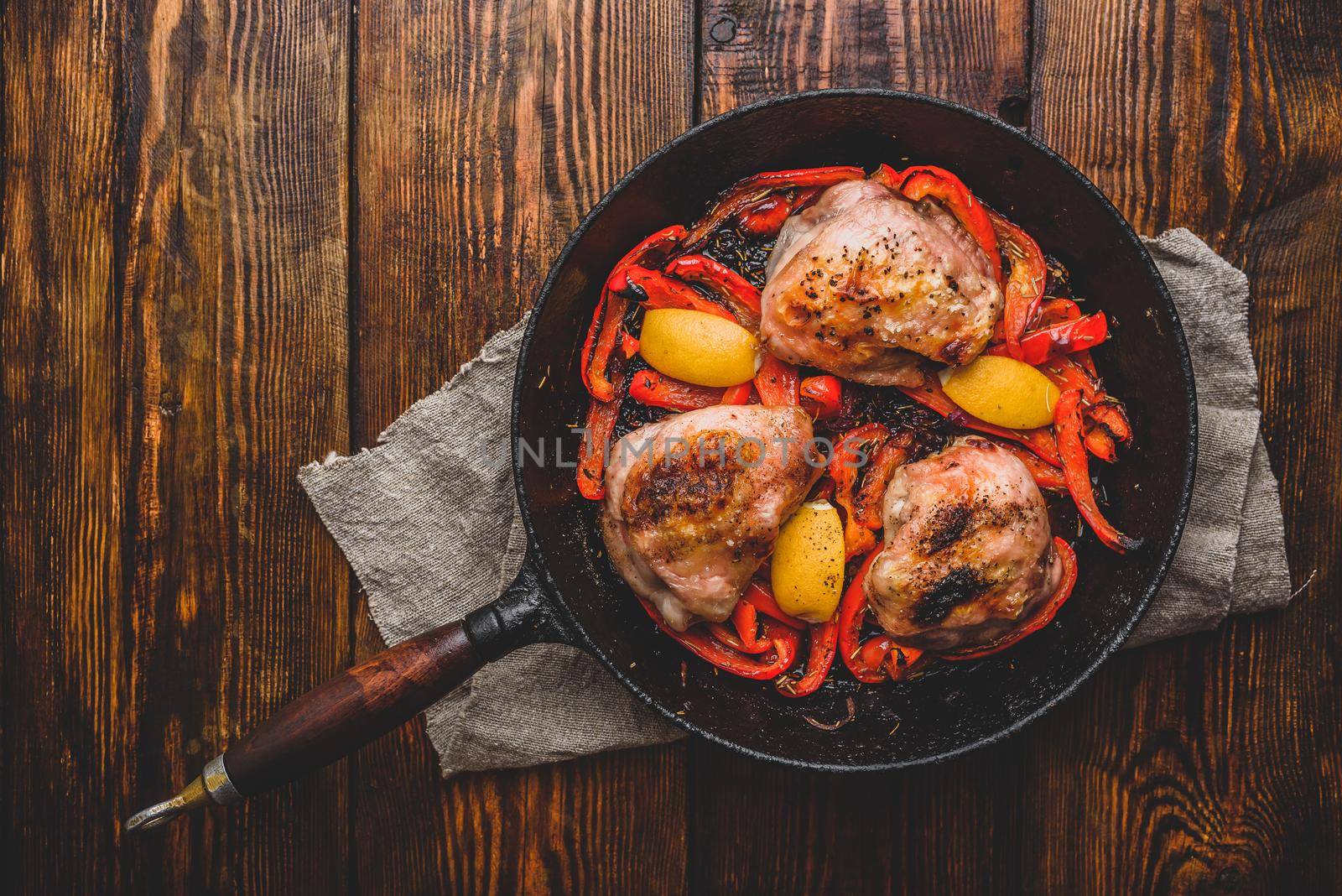 Chicken thighs baked with red bell peppers, rosemary and lemon in cast iron skillet. View from above