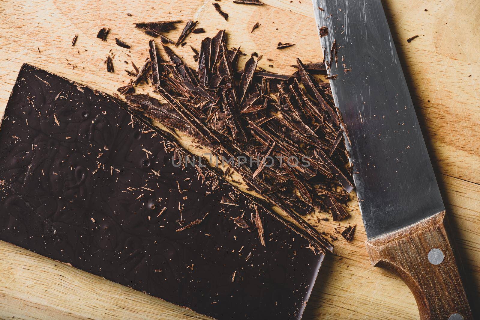 Crushed dark chocolate bar with rustic knife on cutting board
