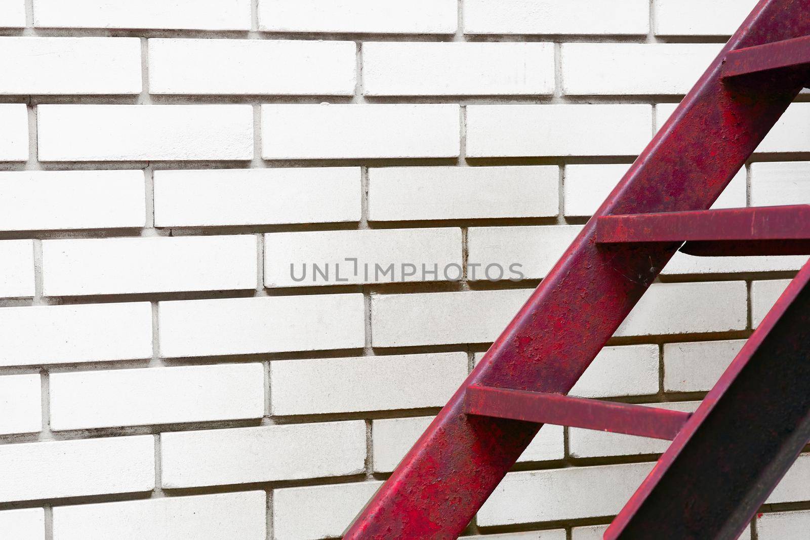 a structure consisting of a series of bars between two upright lengths of wood, metal used for climbing up or down.Part of the stairs red metal ladder leading up against of a white brick wall