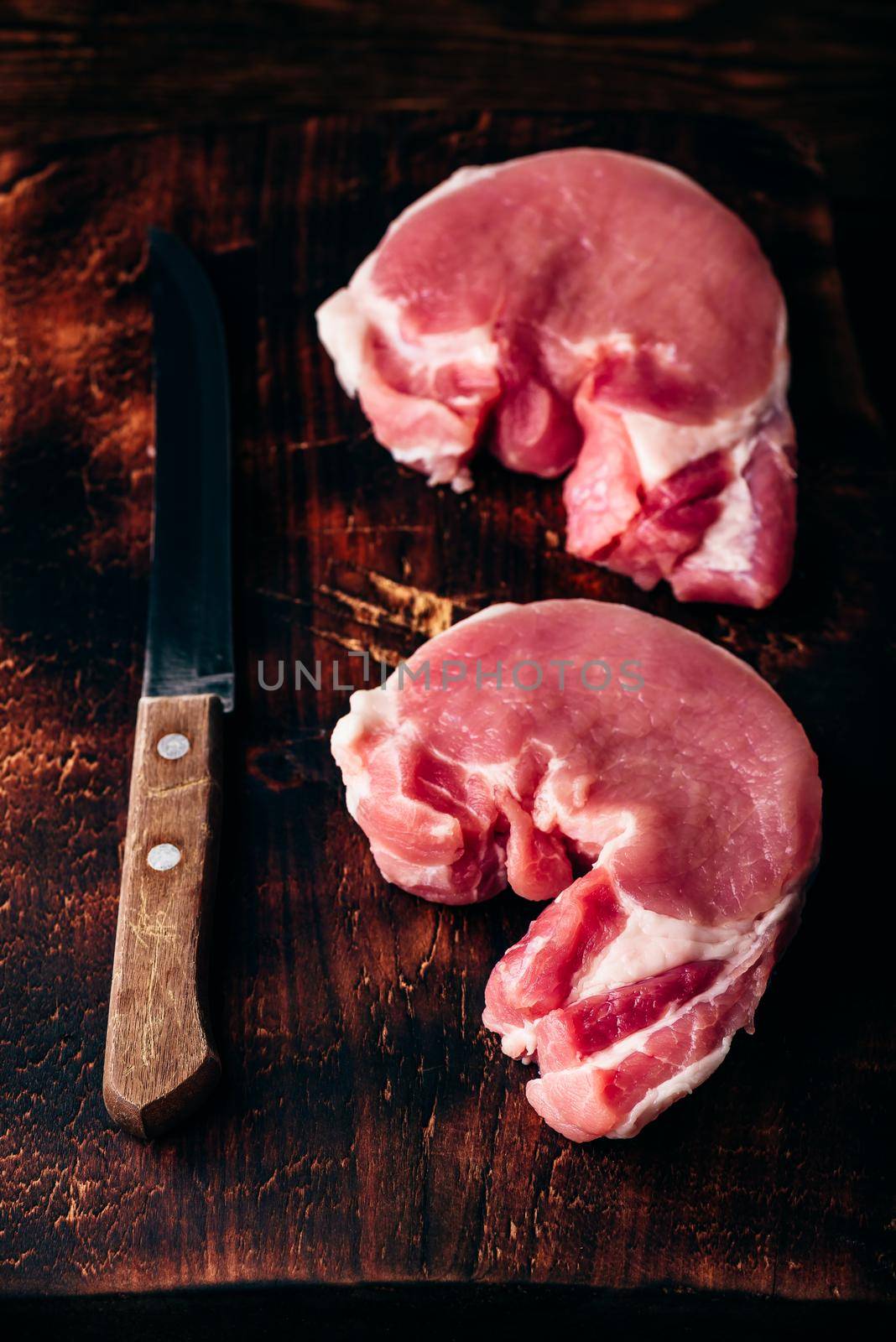 Two pork loin steaks with knife on rustic cutting board