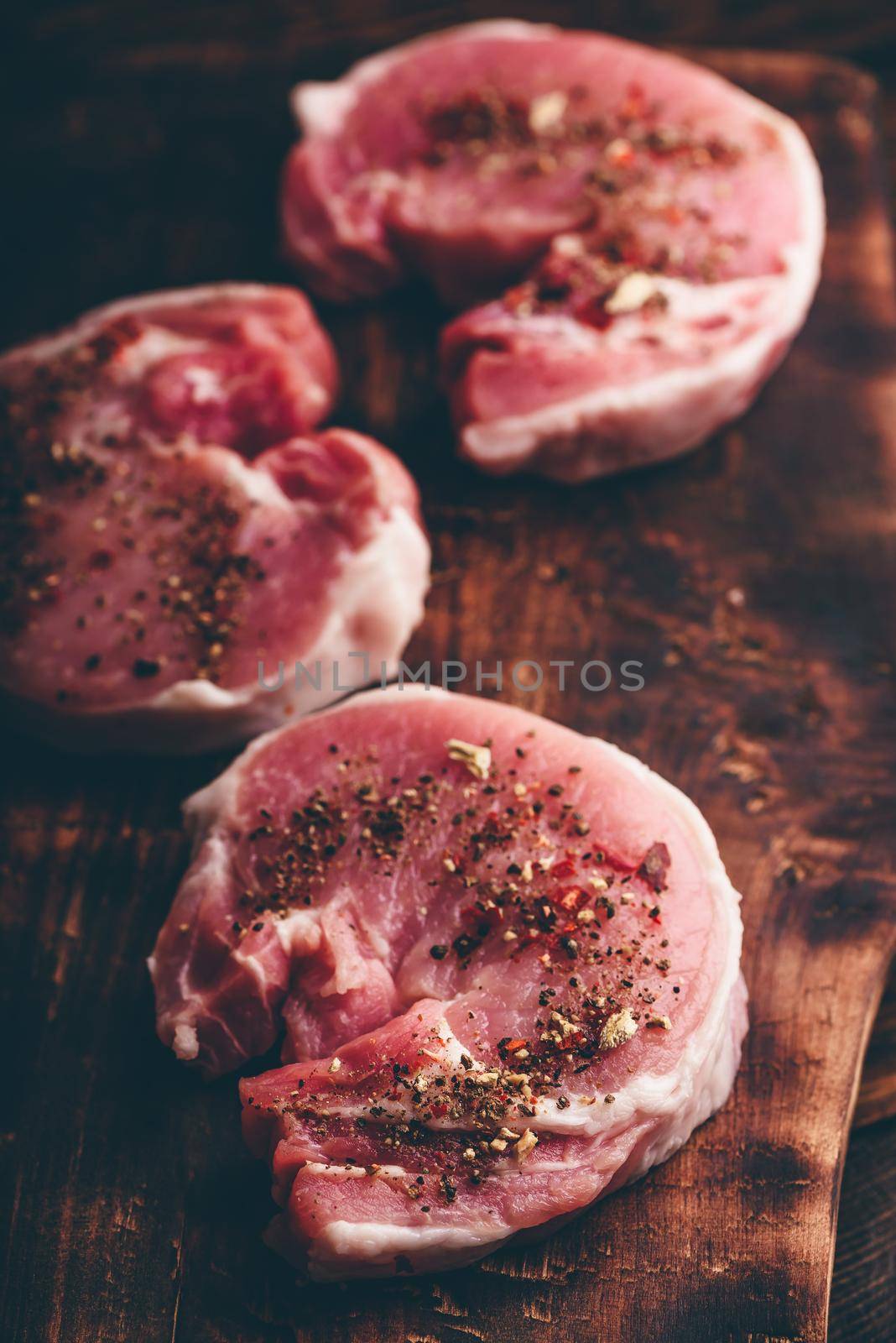 Raw pork loin steaks with different spices on rustic cutting board