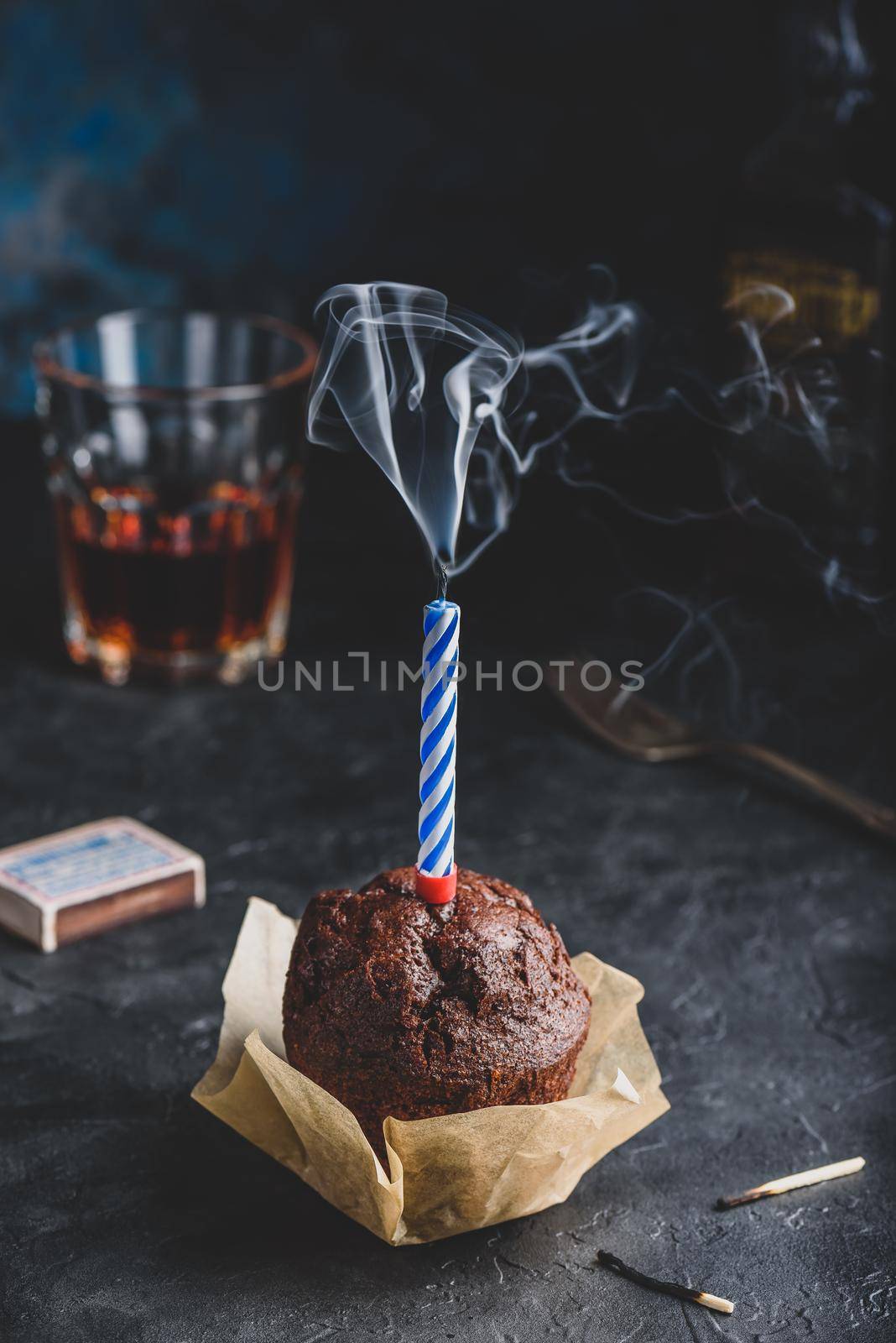 Birthday chocolate muffin with smoking candle on dark concrete background