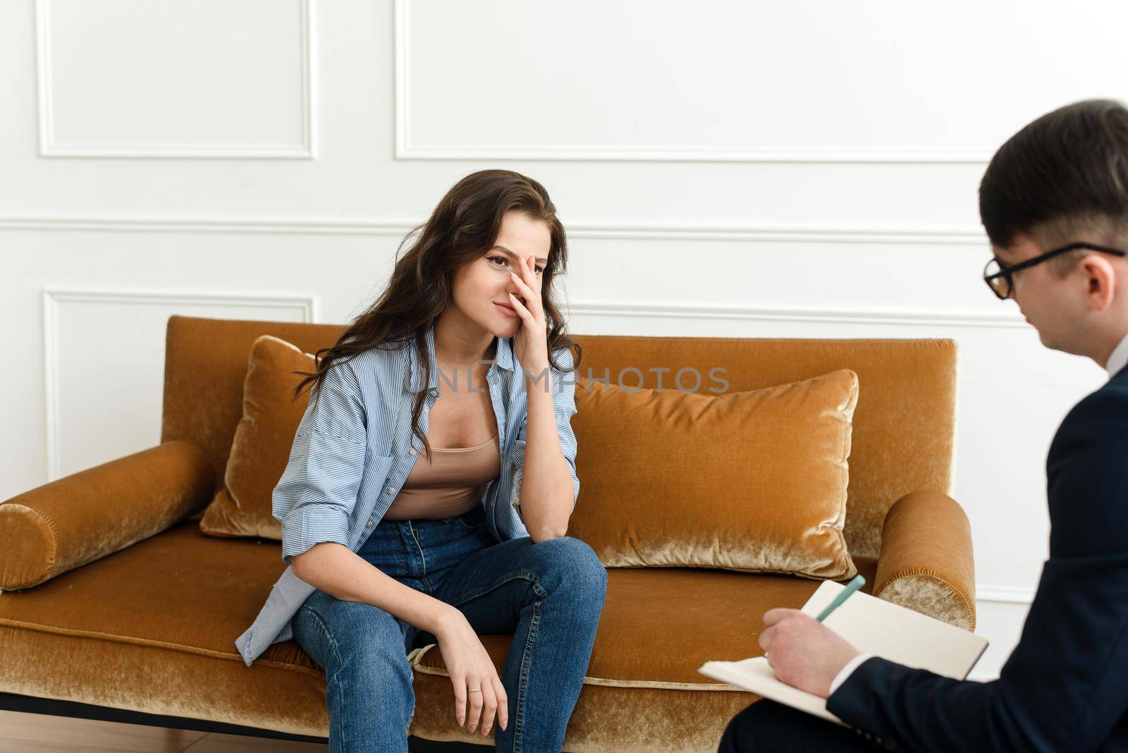 A young woman at a psychiatrist's or psychologist's appointment is worried, holds her hands to her face and tries to talk about her problems