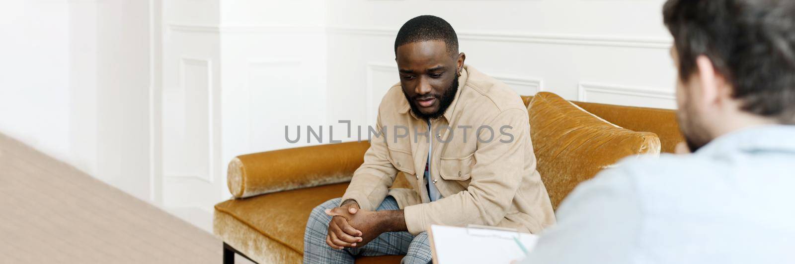 Unhappy young black man gay having session with professional psychologist at mental health clinic. Professional psychological help concept. Web banner.