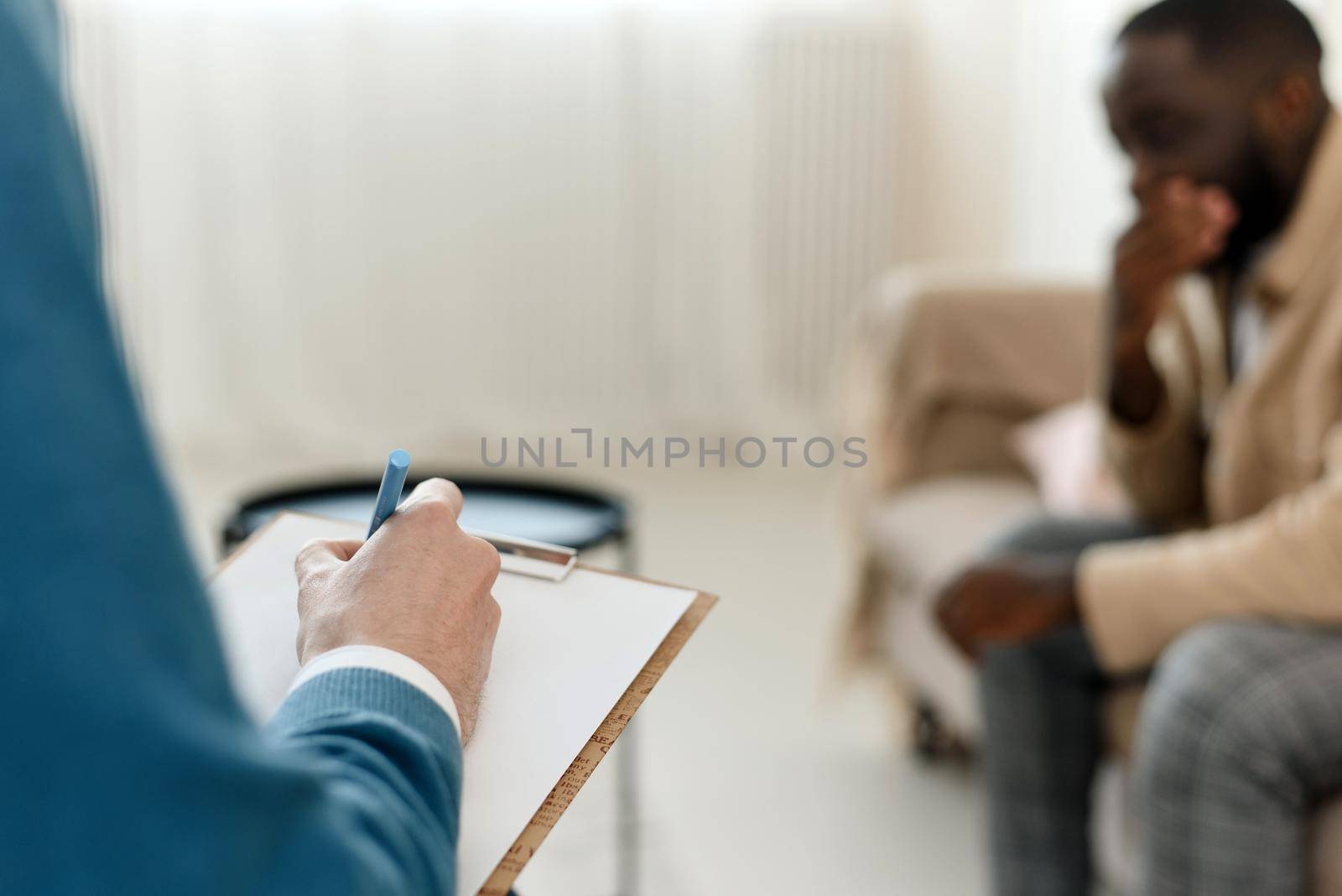 The therapist takes notes while talking to a depressed male patient and talks to an African American patient. Desperate black man suffering from nervous breakdown or depression having a session with a psychologist.