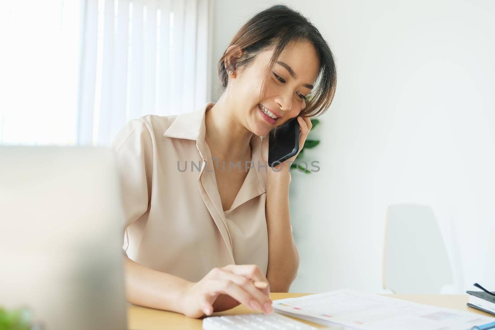 new normal, a businesswoman using computer and smartphone to work for a company Via the internet on your desk at home. by Manastrong