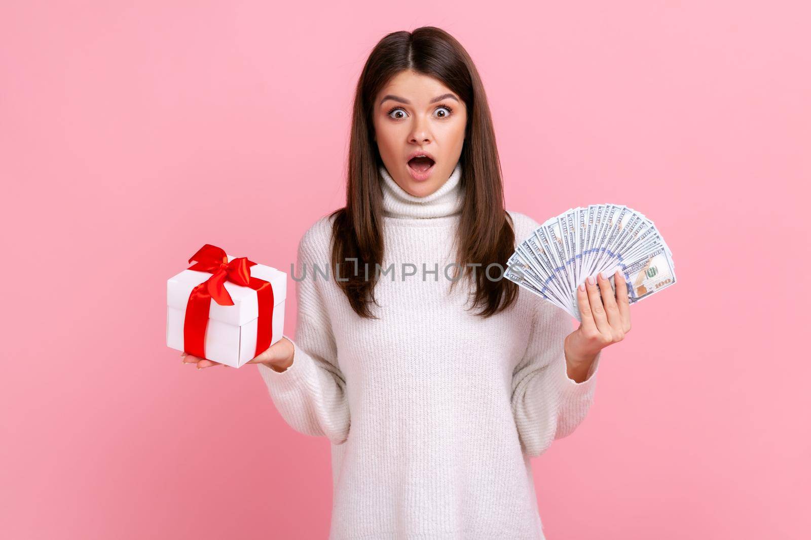 Shocked brunette woman with dark hair holding wrapped present box and big fan of dollar banknotes. by Khosro1