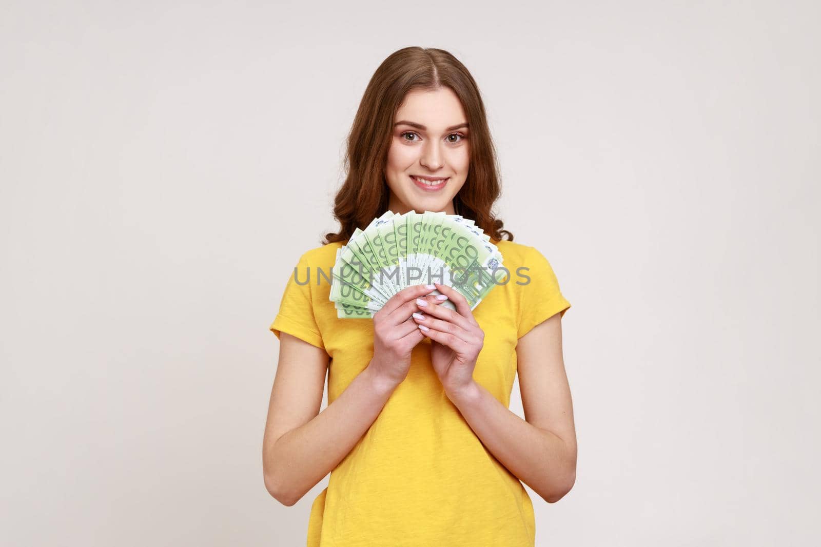 Rich beautiful woman of young age with brown wavy hair in yellow casual style T-shirt showing euro banknotes, high salary, big profit. by Khosro1