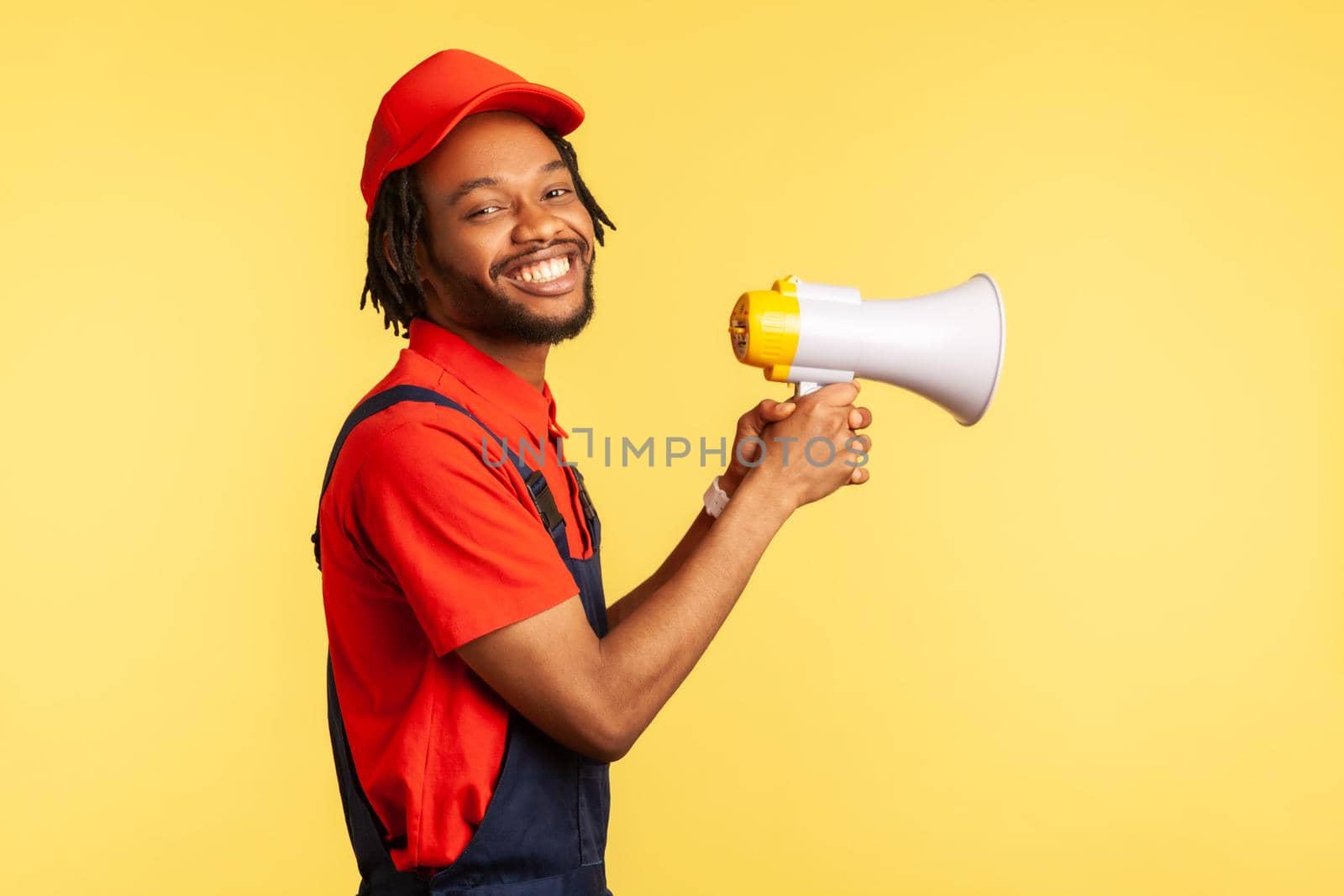 Handyman wearing blue overalls and red cap, holding megaphone, looking at camera with toothy smile. by Khosro1