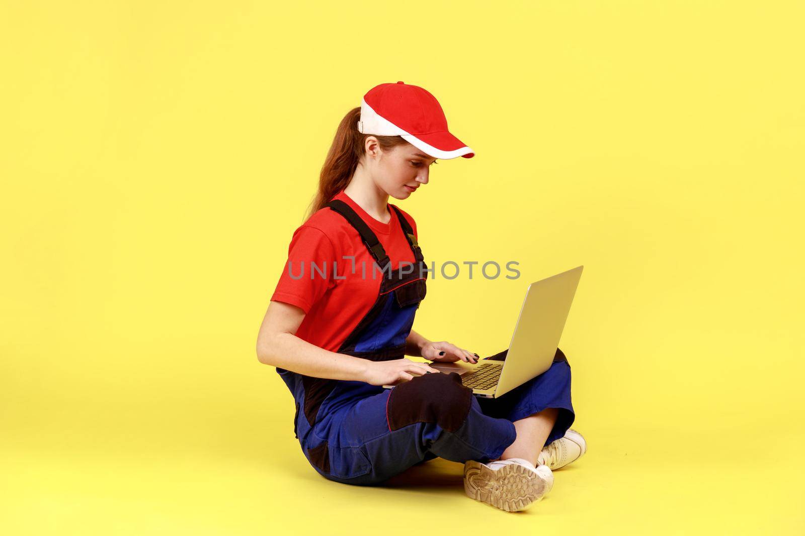 Concentrated handy woman sitting on floor and working on laptop, looking at display while typing. by Khosro1